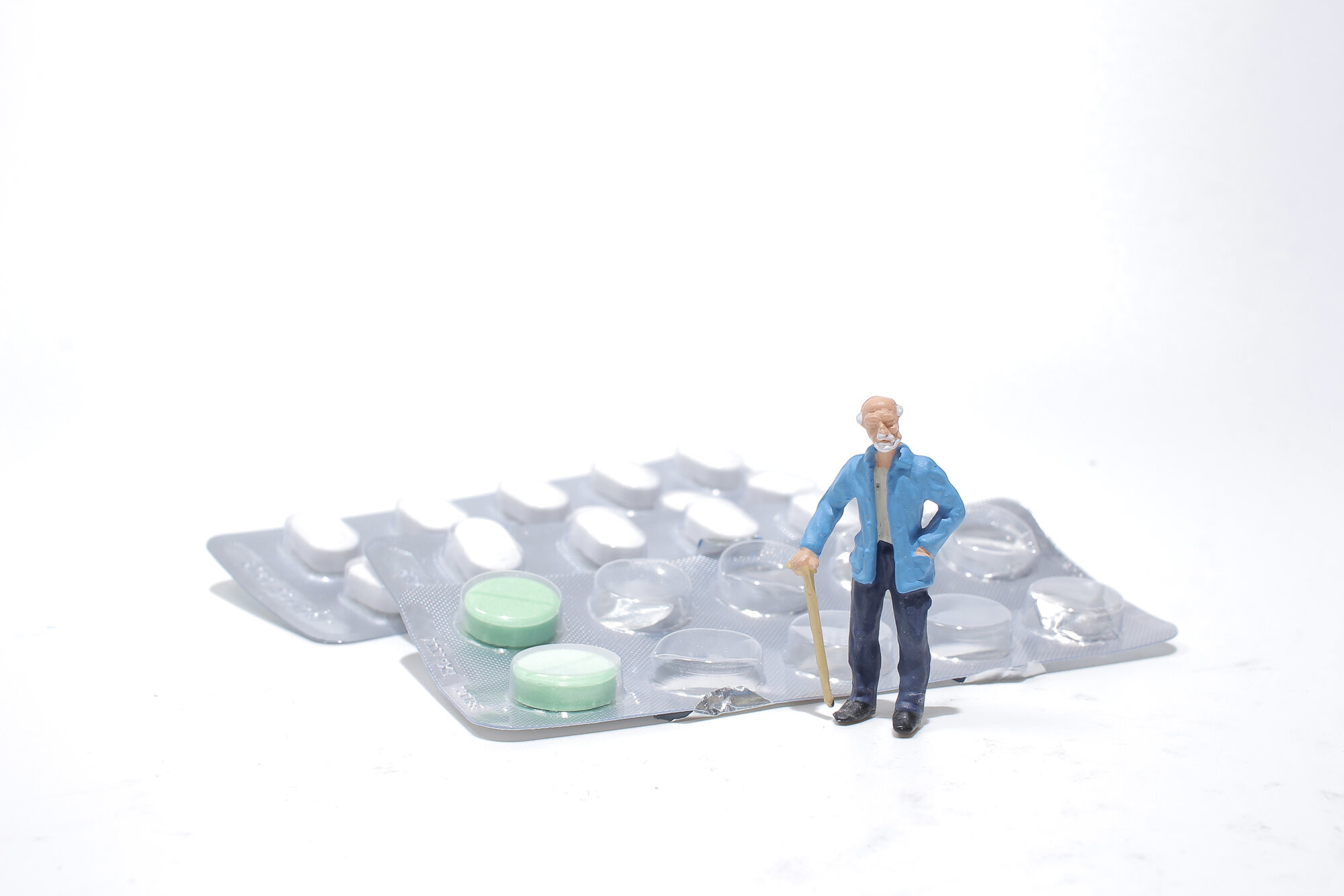 Bildet viser en figur av en eldre mann som står ved siden av et brett med medisiner