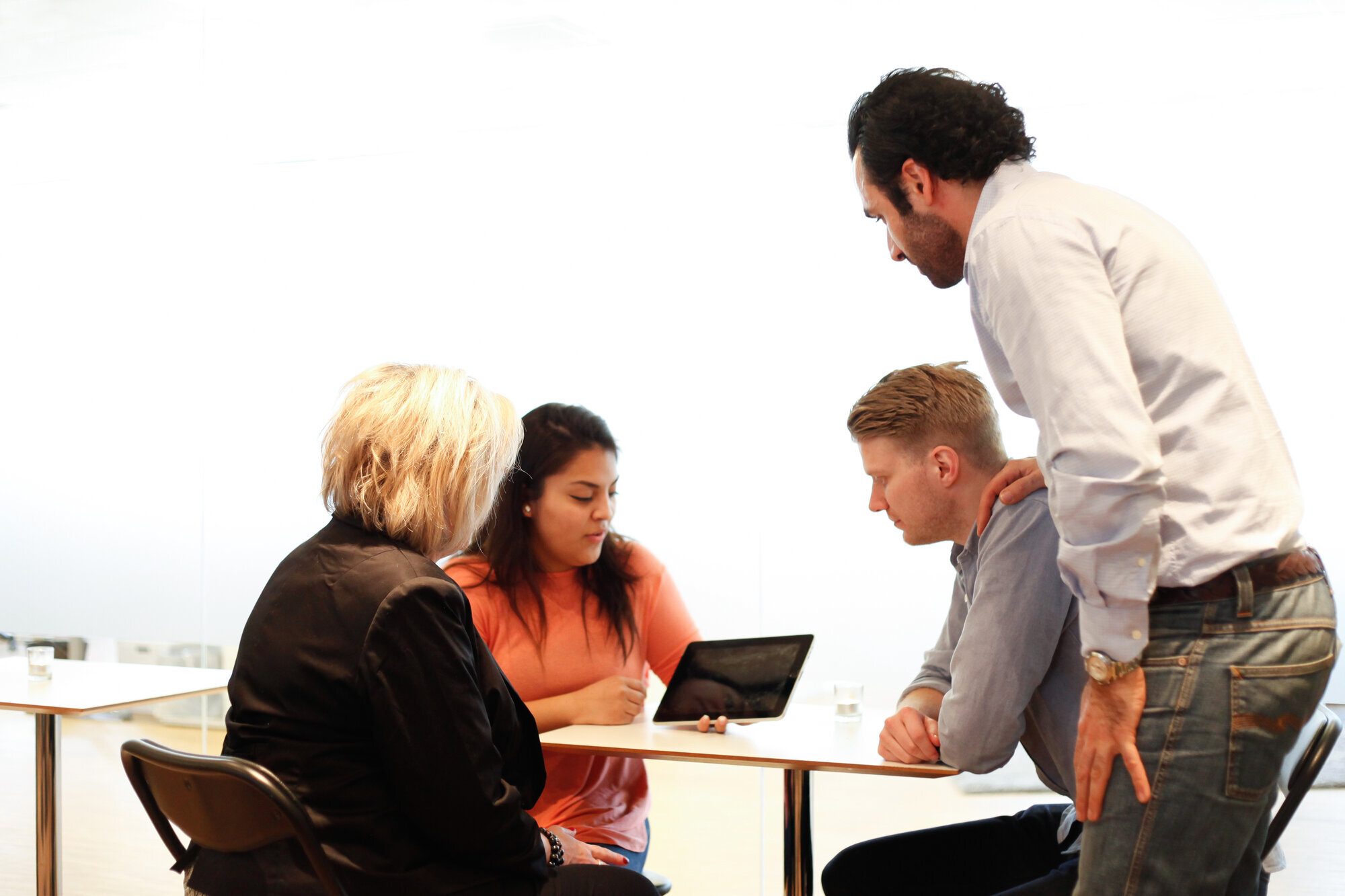 Bildet viser møtedeltakere rundt et bord. En mann holder står oppe og holder hånda støttende på skulderen til en yngre mann