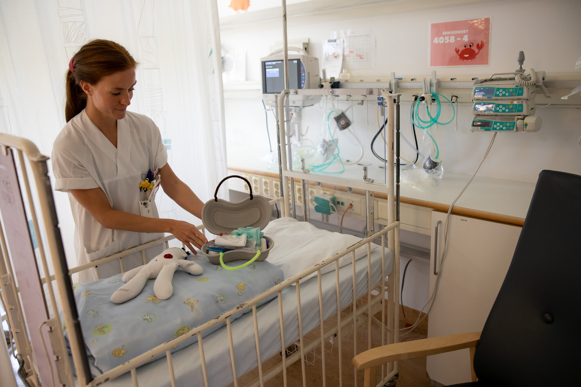 Bildet viser en sykepleier som legger frem en dukke og et førstehjelpsskrin laget av pussbekken.