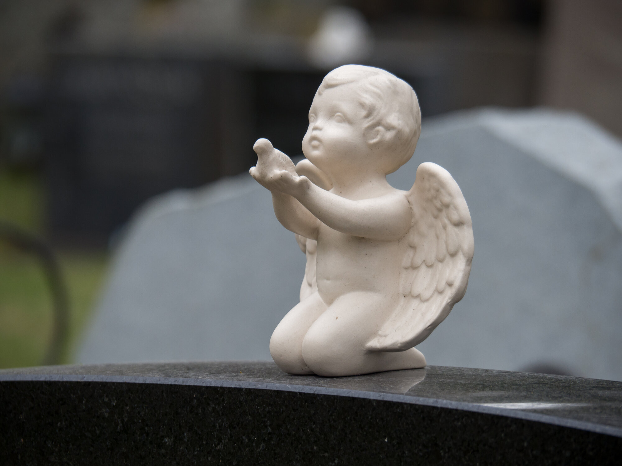 Bildet viser en gravstøtte pyntet med en hvit engel som strekker ut armene.