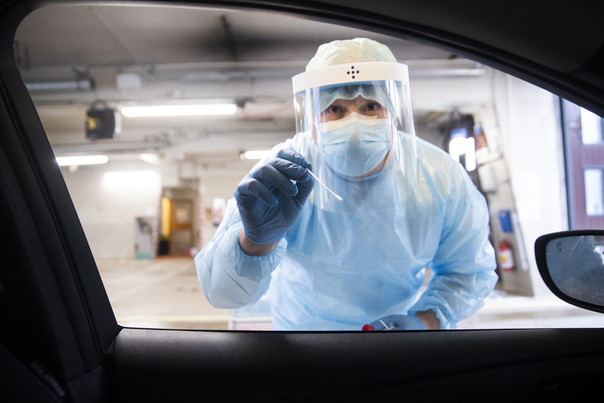 Bildet viser en helsearbeider i smittevernutstyr som holder frem en testpinne.