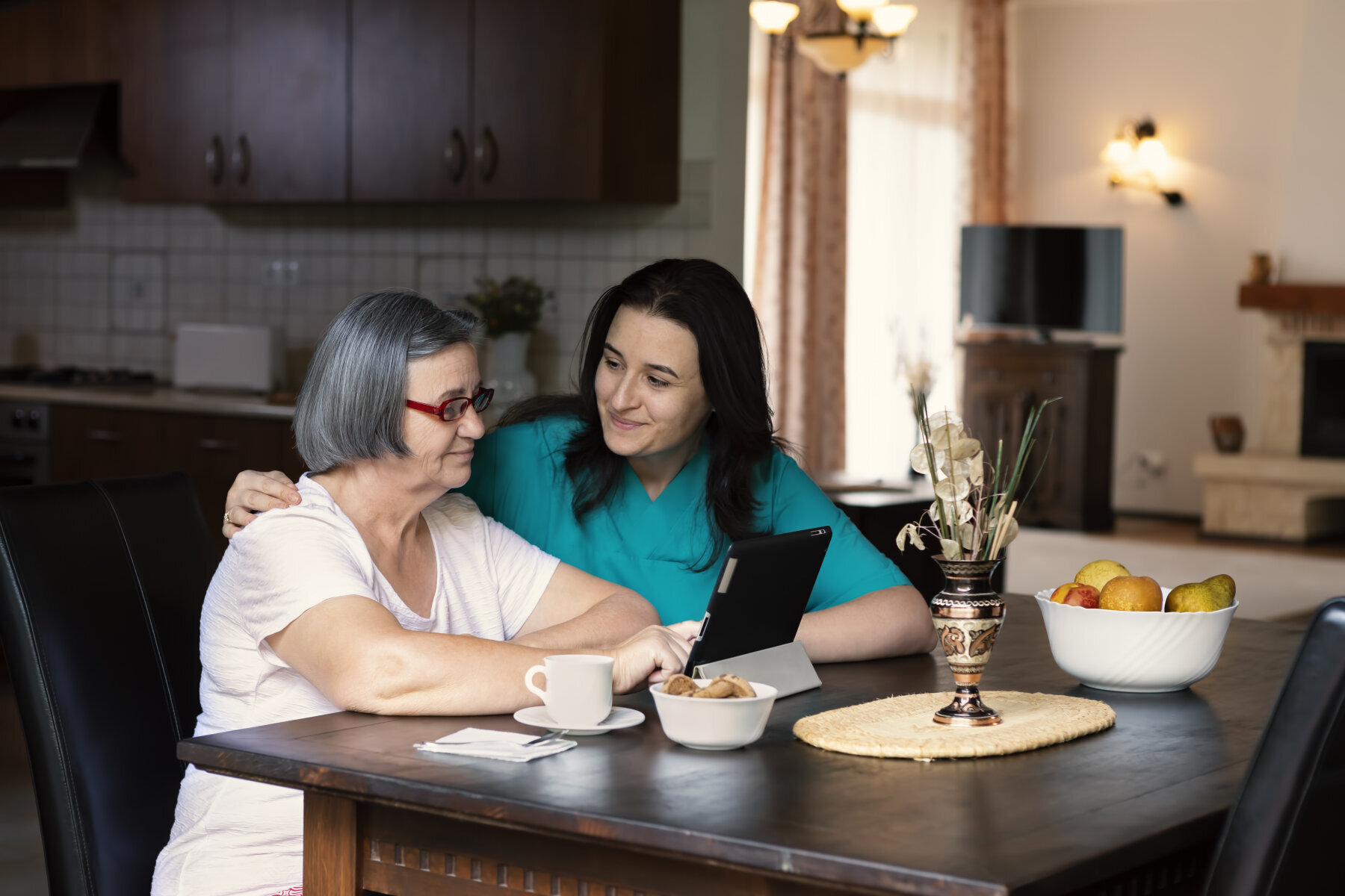 Bildet viser et helsepersonell som holder rundt en eldre kvinne som ser på et nettbrett