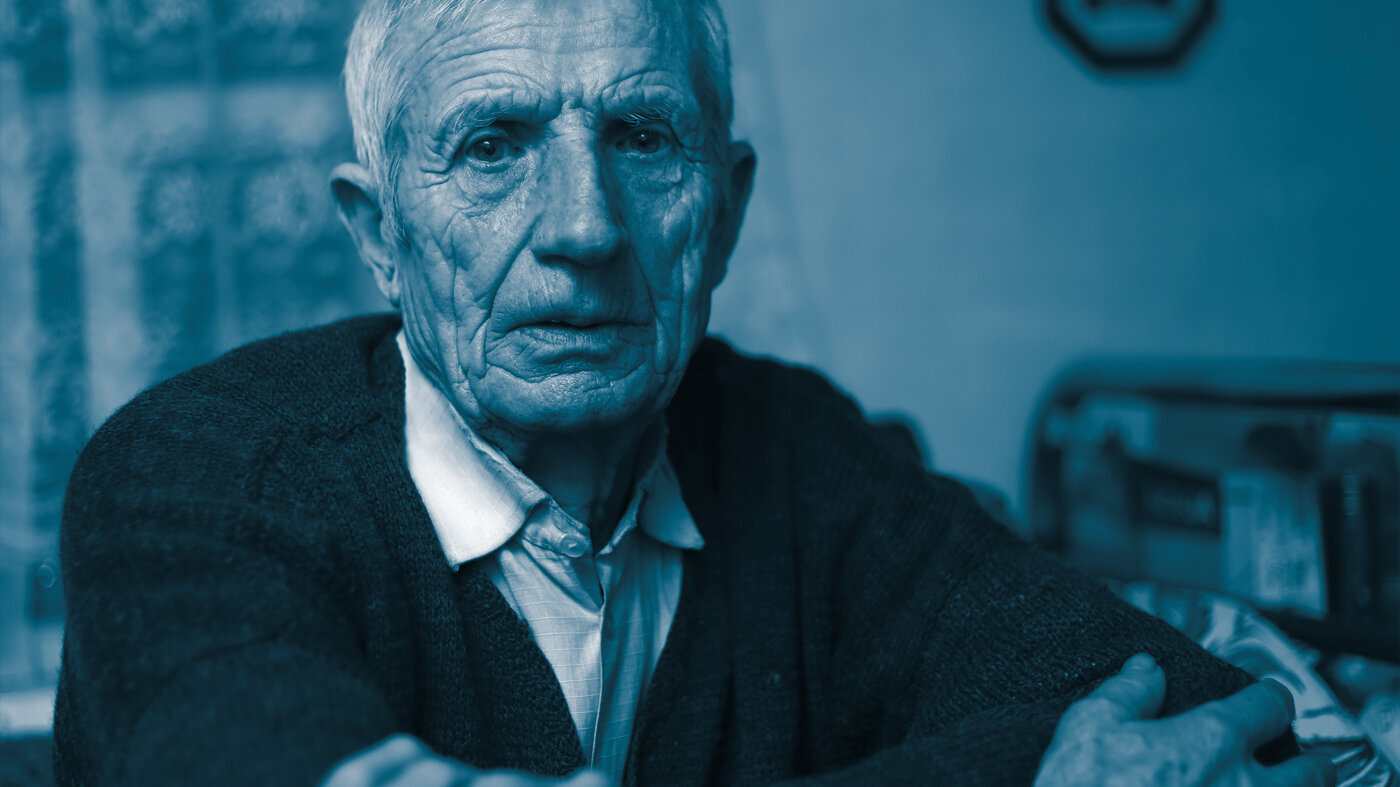 The photo shows a close-up of an older man looking straight at the camera. He looks sad.