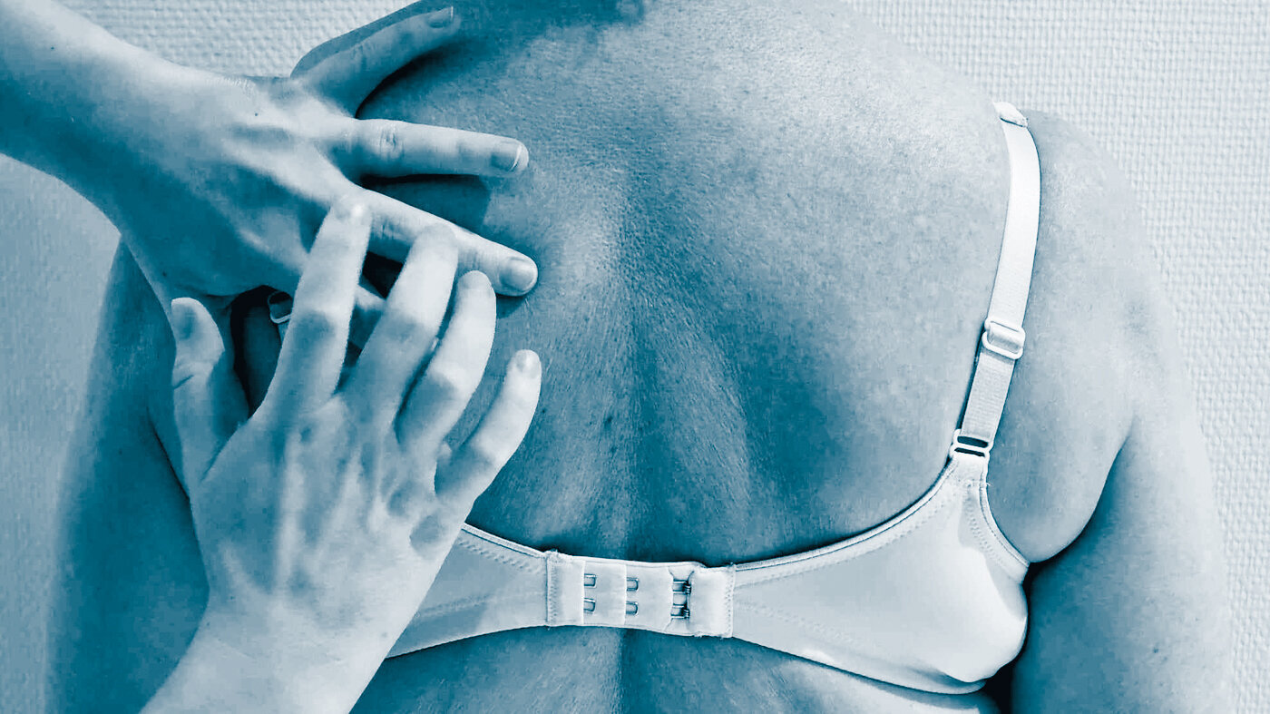 The photo shows the back of a woman wearing a bra. A nurse knocks her fingers on the woman's back, listening to her lungs, performing percussion.