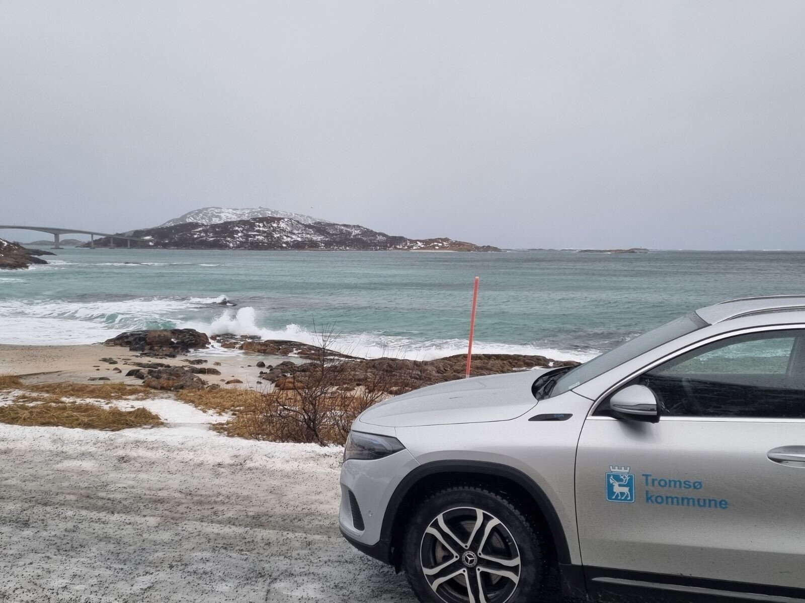 Bildet viser en bil parkert nede ved havet med Sommerøybrua og Sommerøy i bakgrunnen. Bildet viser en bil parkert nede ved havet med Sommerøybrua og Sommerøy i bakgrunnen