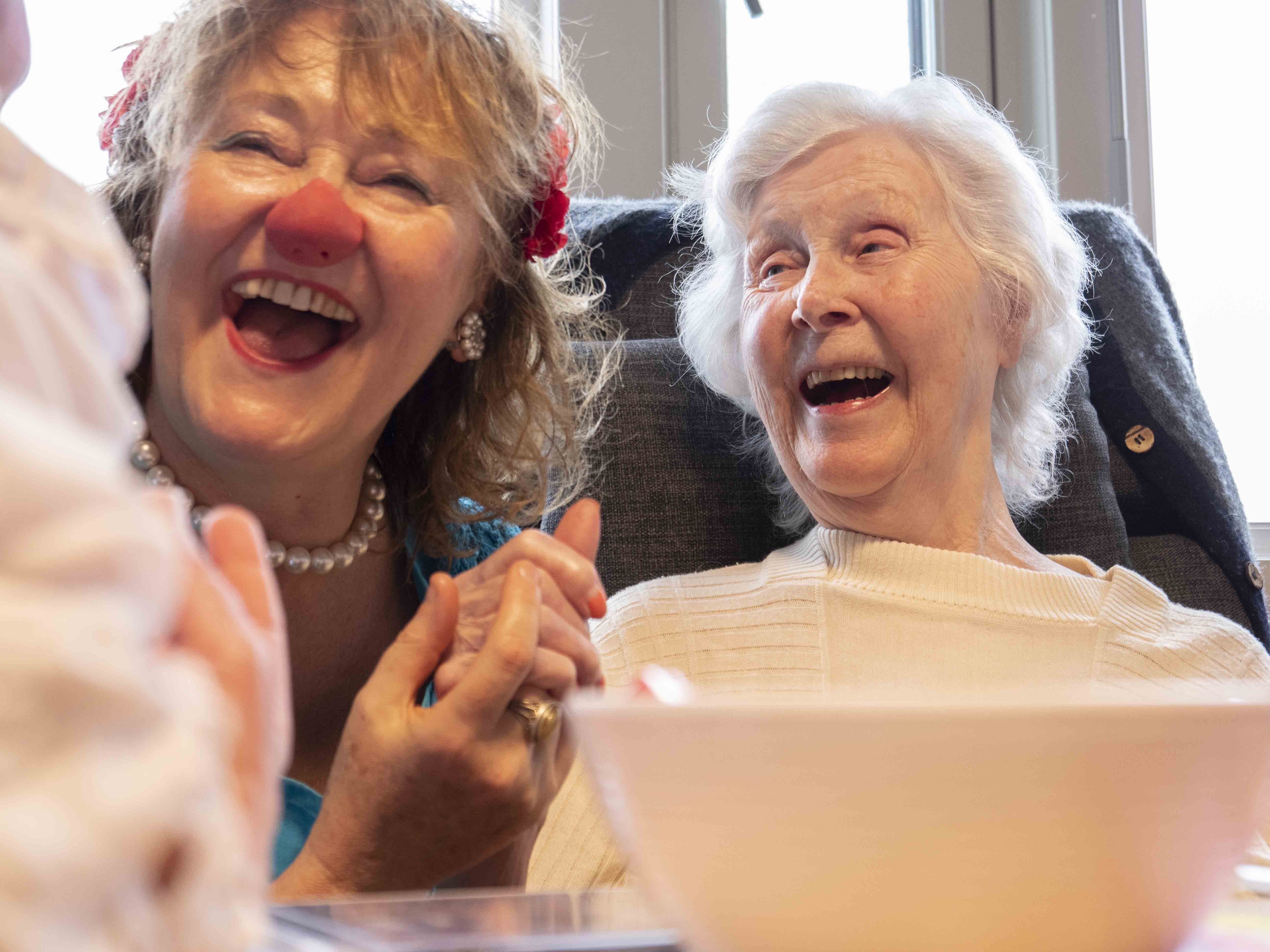 Bildet viser en klokkeklovn på et sykehjem sammen med en eldre kvinne. Kvinnen ler.