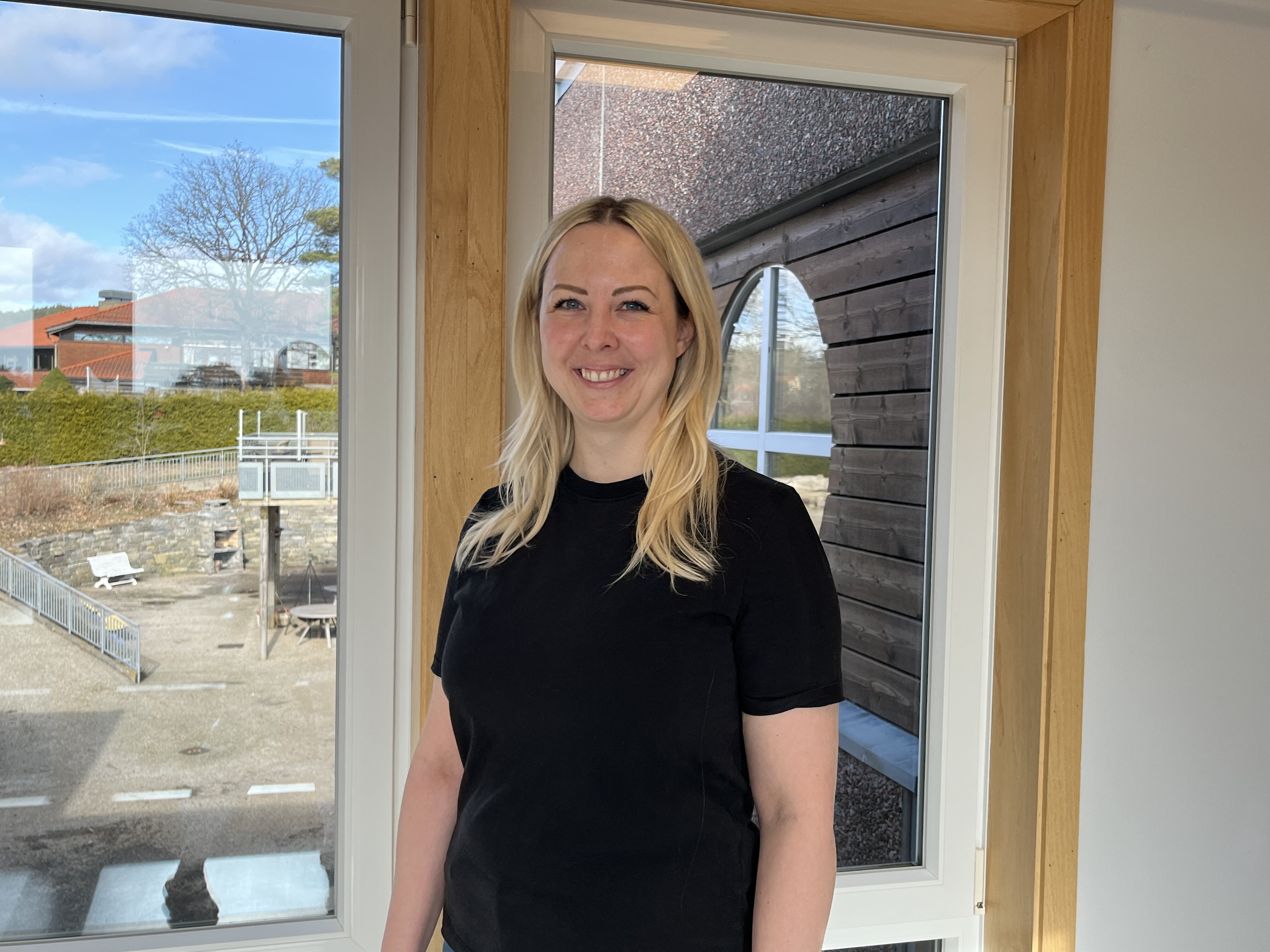 Bildet viser Helene Herlandsen. Hun står foran et vindu og smiler til kamera