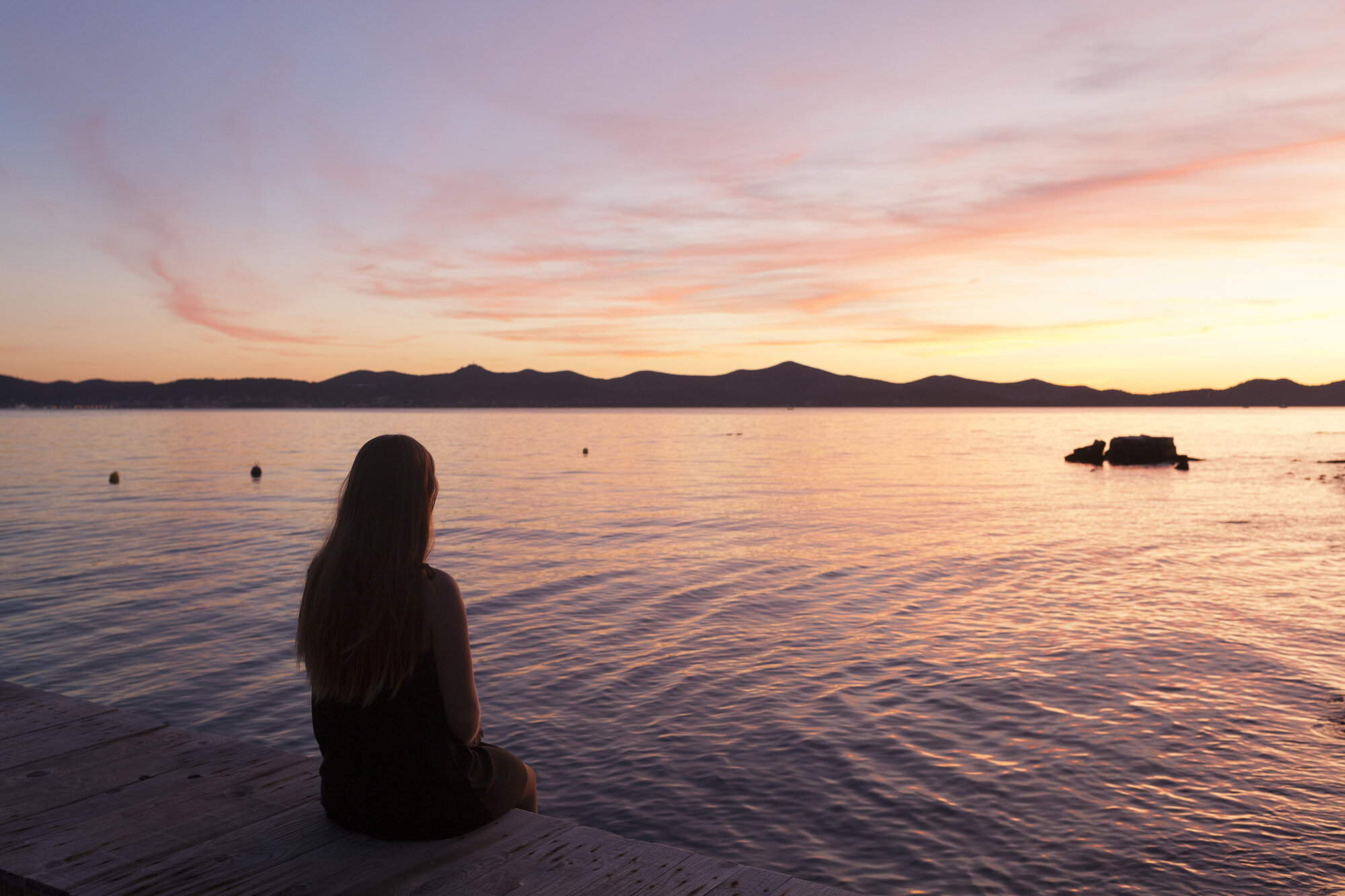 Bildet viser en ung kvinne som sitter med ryggen til og ser utover vannet