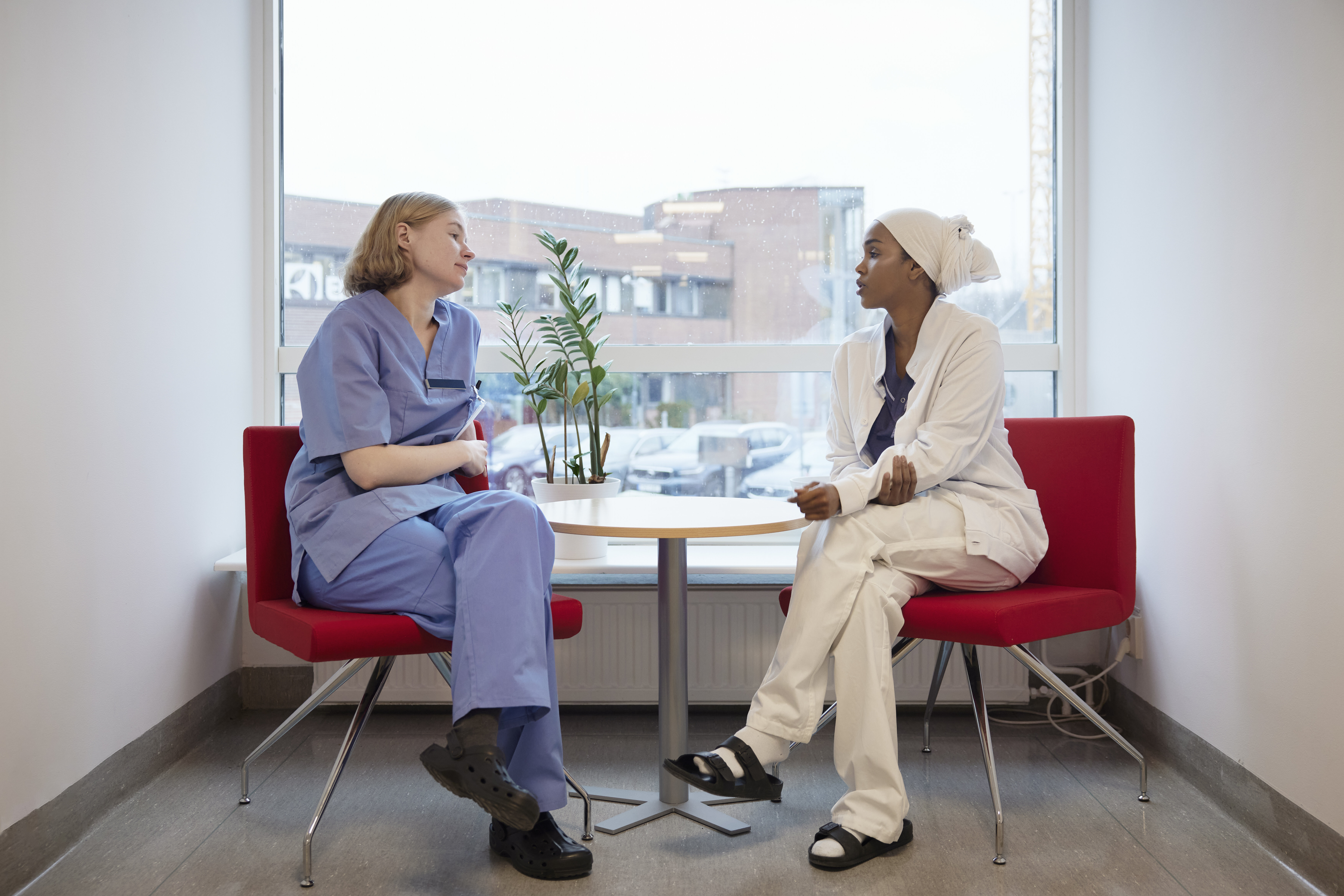 The photo shows two nurses sitting and talking together in front of a window
