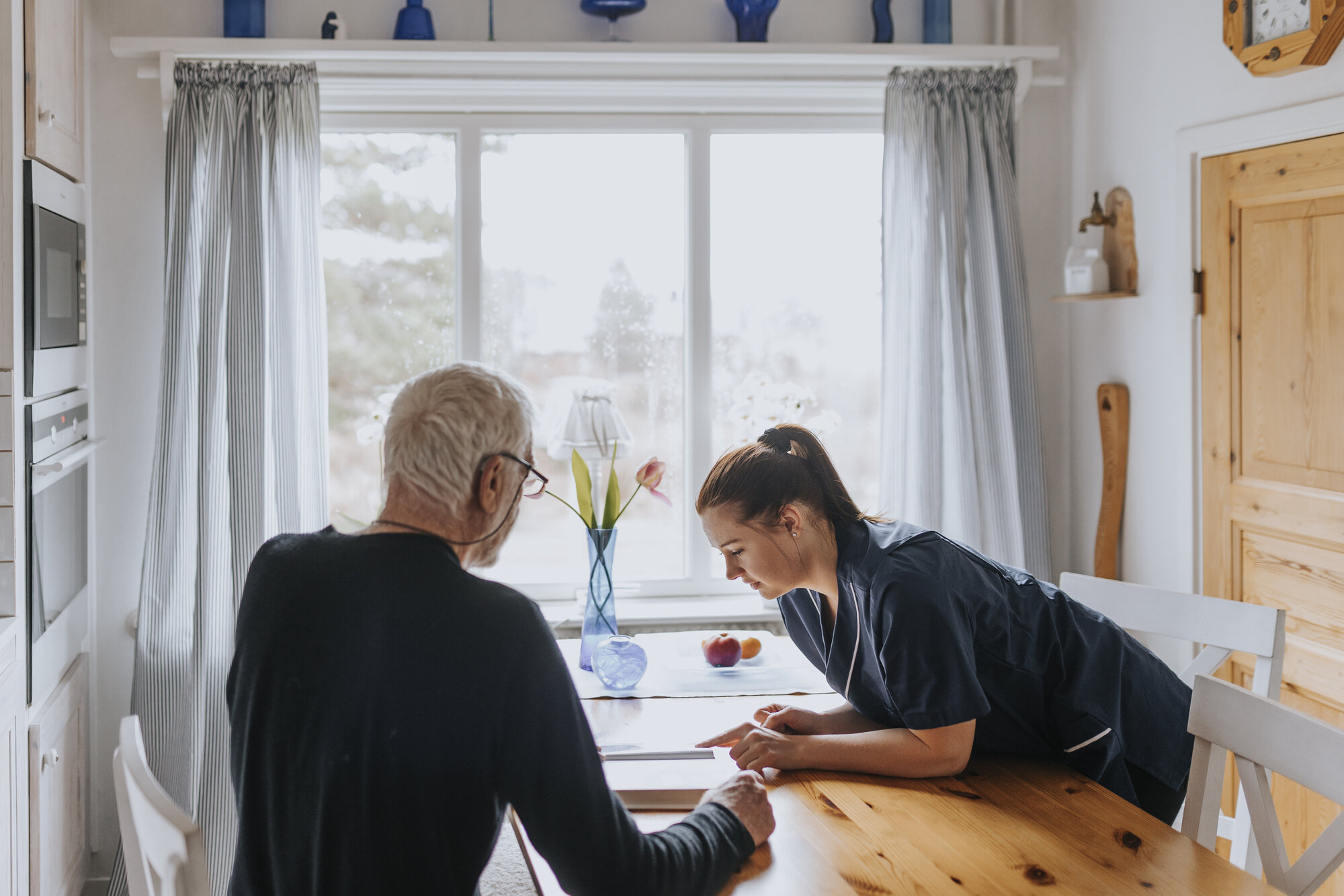 Bildet viser en hjemmesykepleier og en eldre mann på kjøkkenet