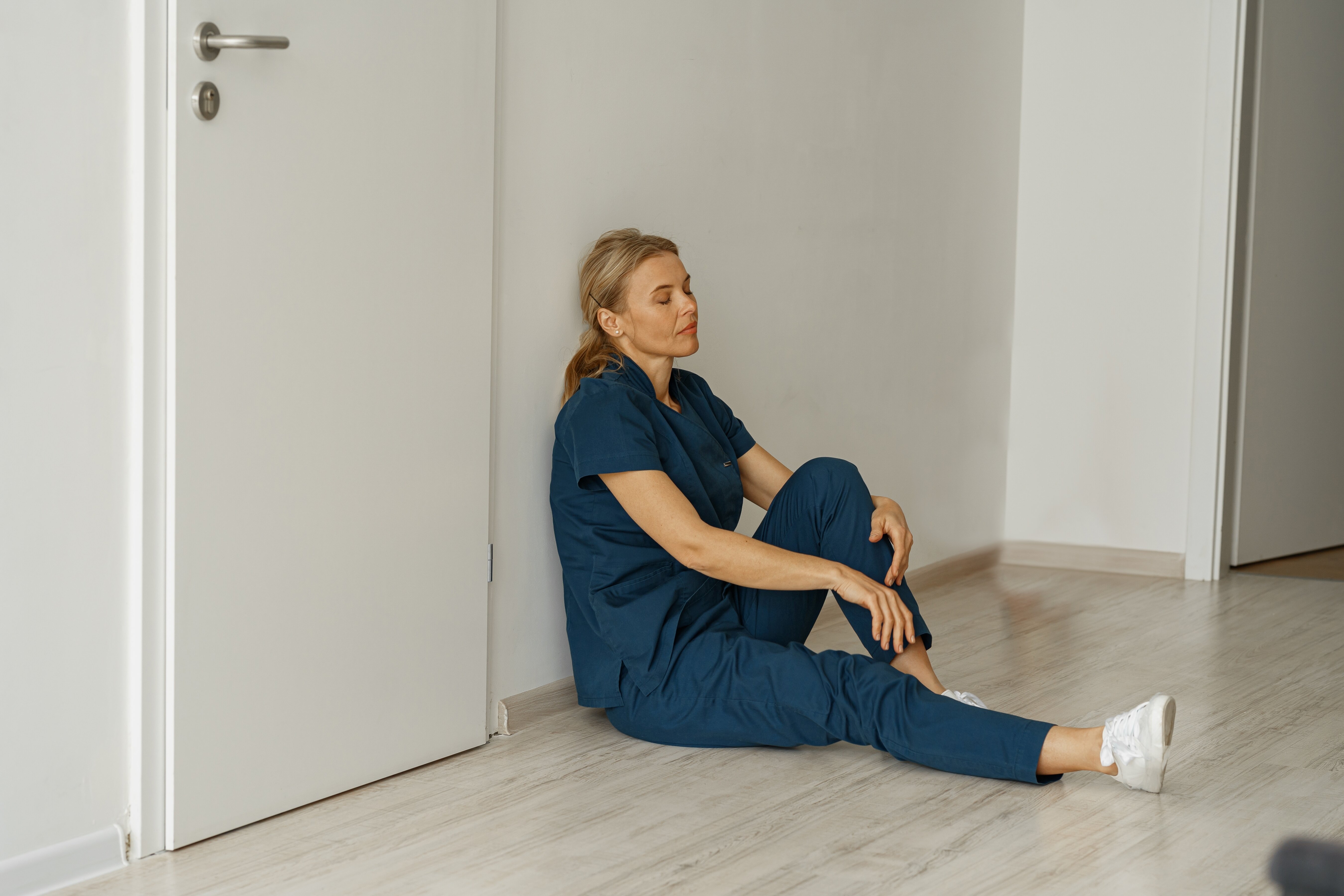 The photo shows a tired nurse sitting on the floor leaning against the wall.