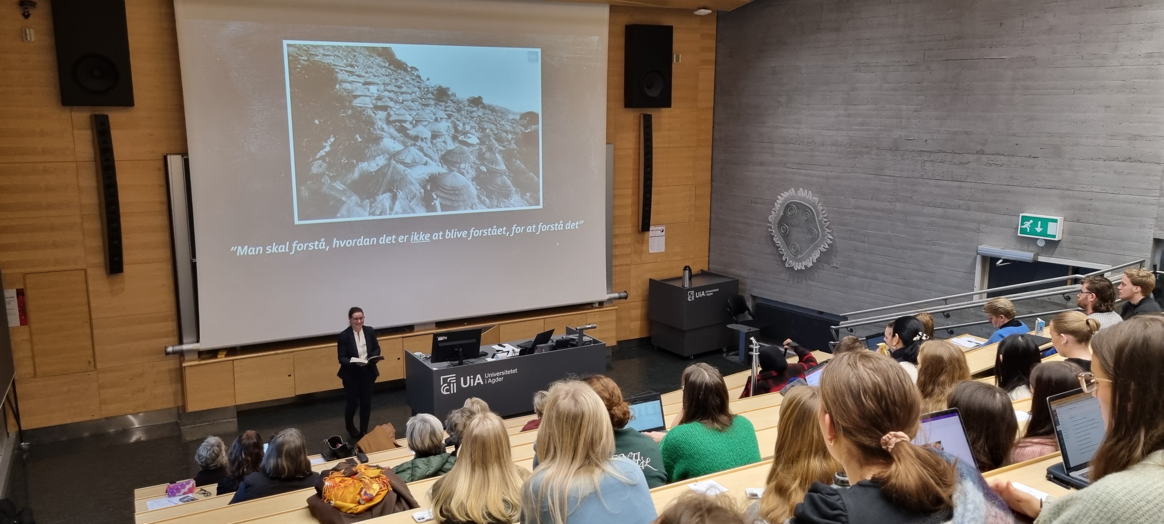 Bildet viser en foreleser som står foran mange studenter