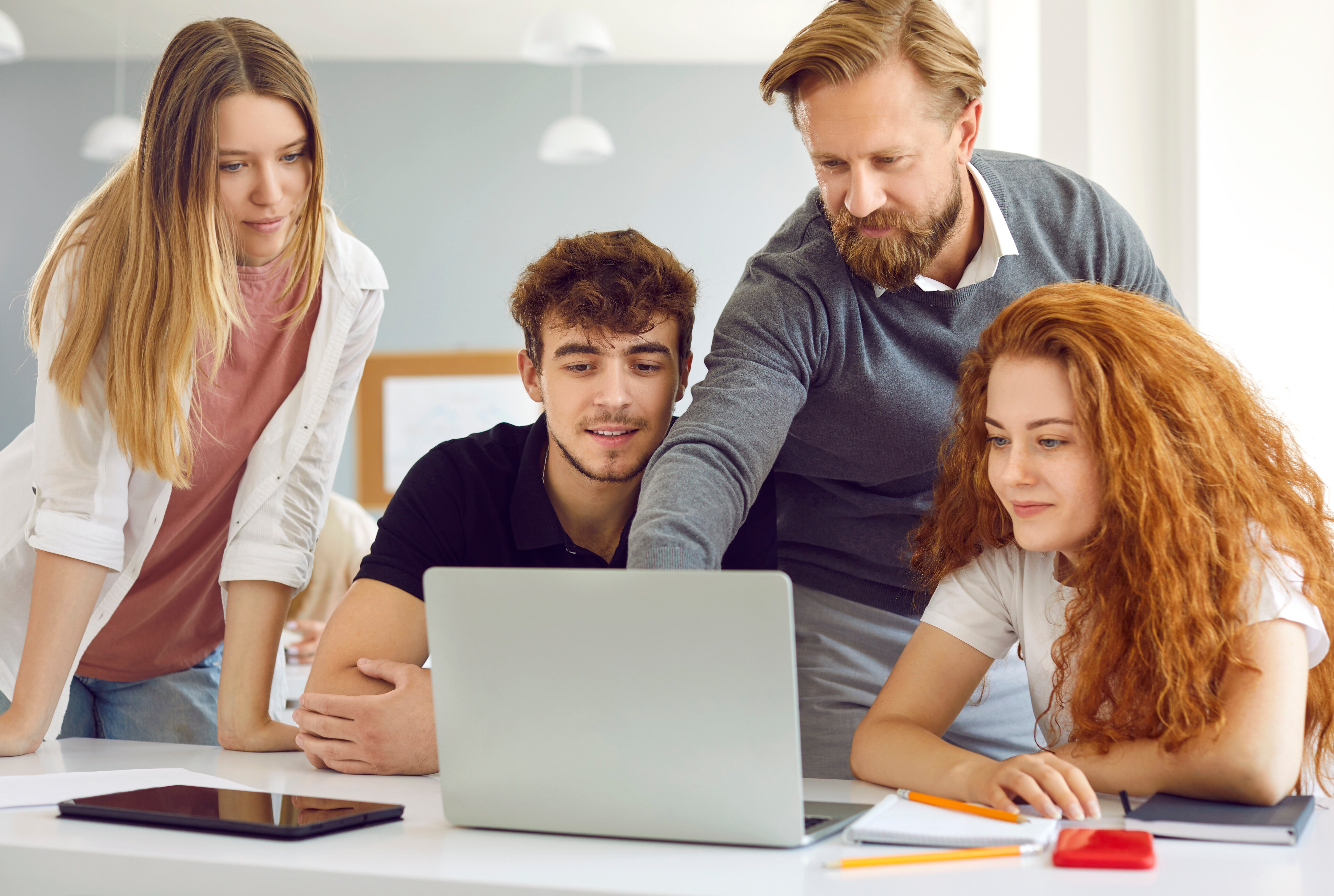Tre studenter og en lærer ser på en dataskjerm sammen