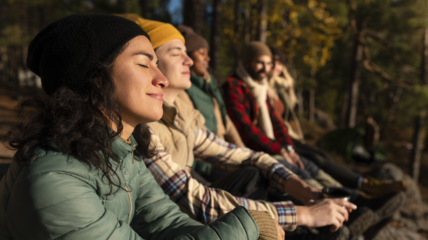 Bildet viser flere mennesker som sitter ute og nyter naturen i stillhet.