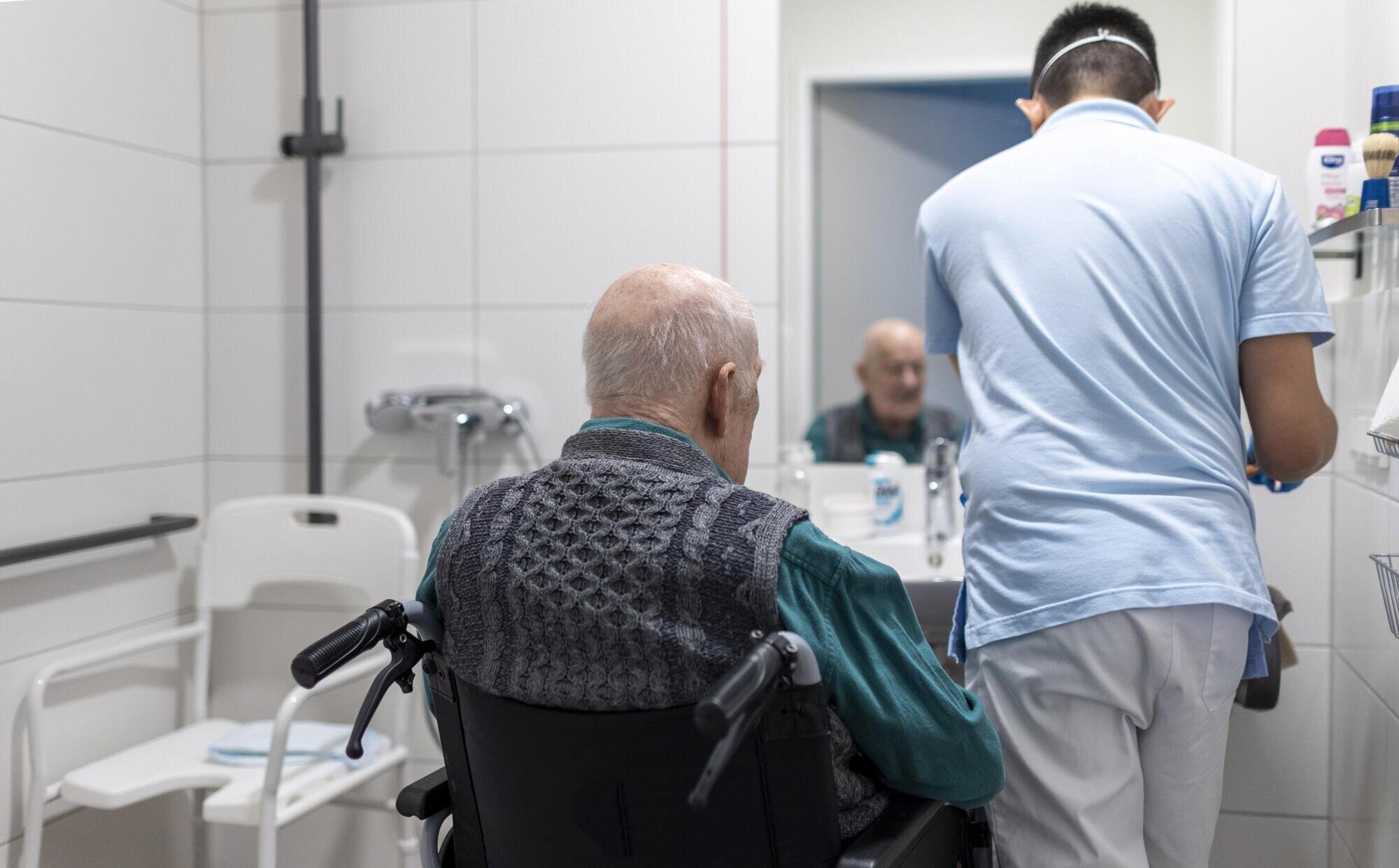 Bildet viser en mannlig sykepleier som steller en eldre pasient på badet