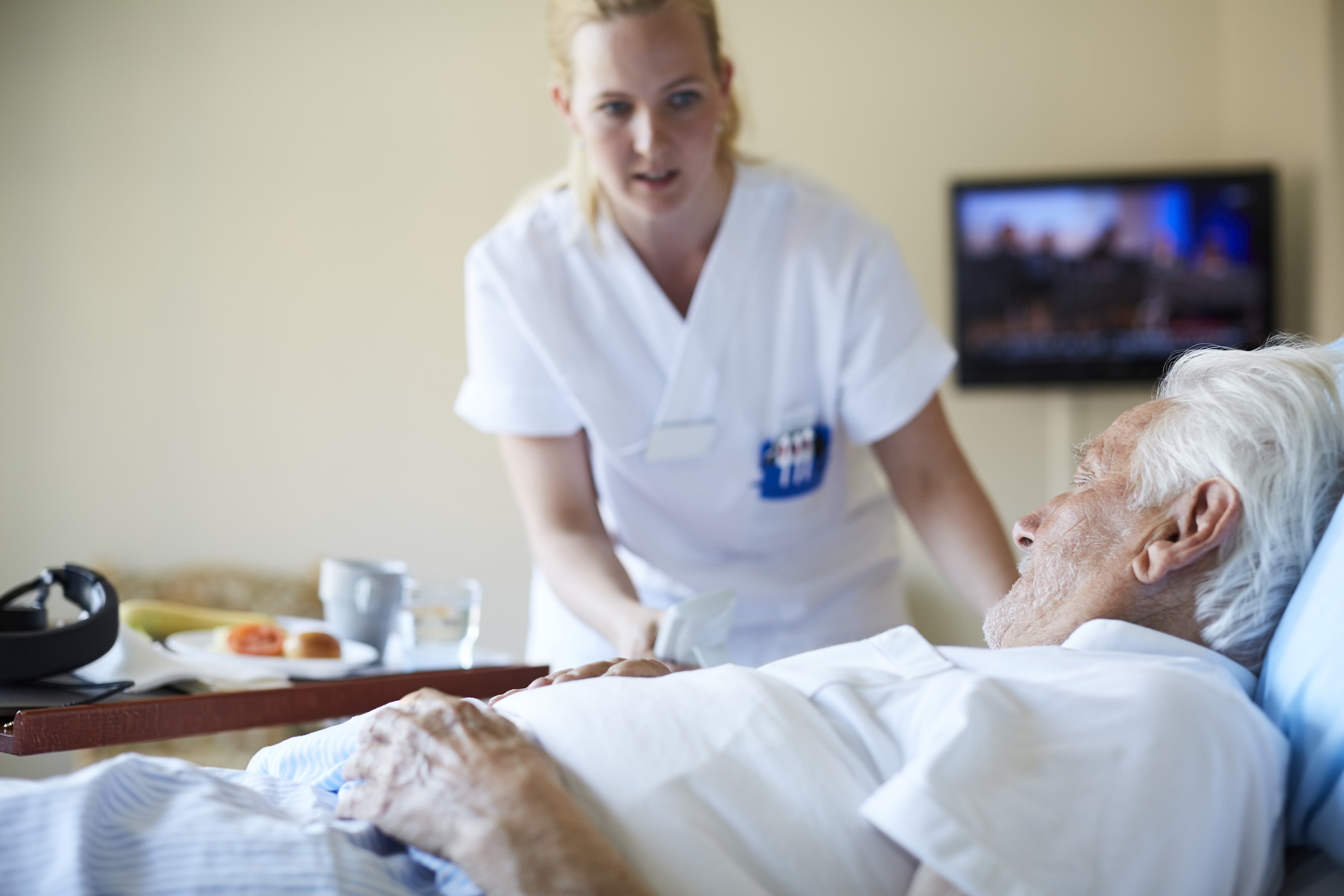 The photo shows a nurse bending over a bed where an older man lies.