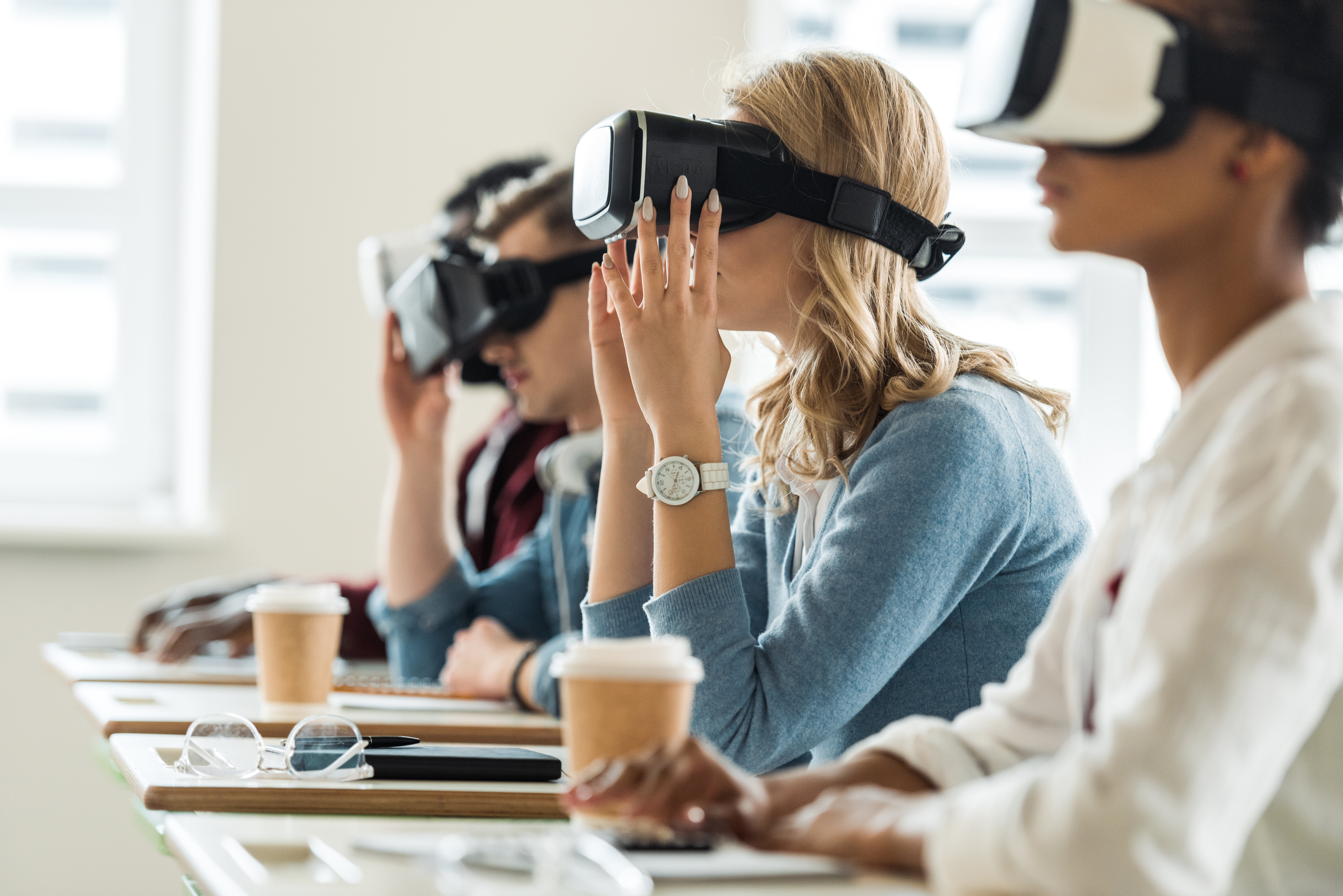 The image shows students with VR glasses. They are sitting by their desks in a class room