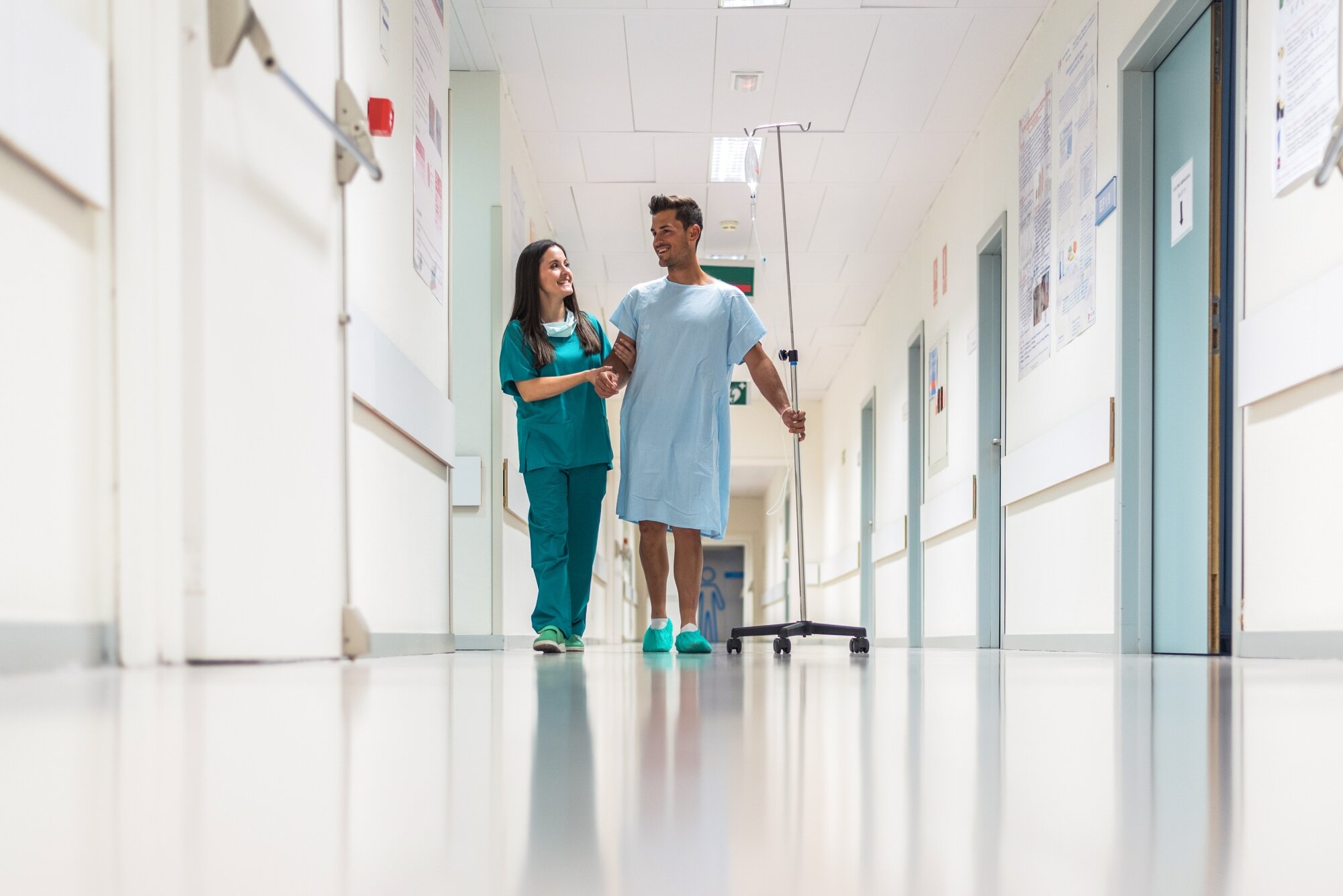 Bildet viser en sykepleier og en pasient som går i sykehuskorridoren sammen