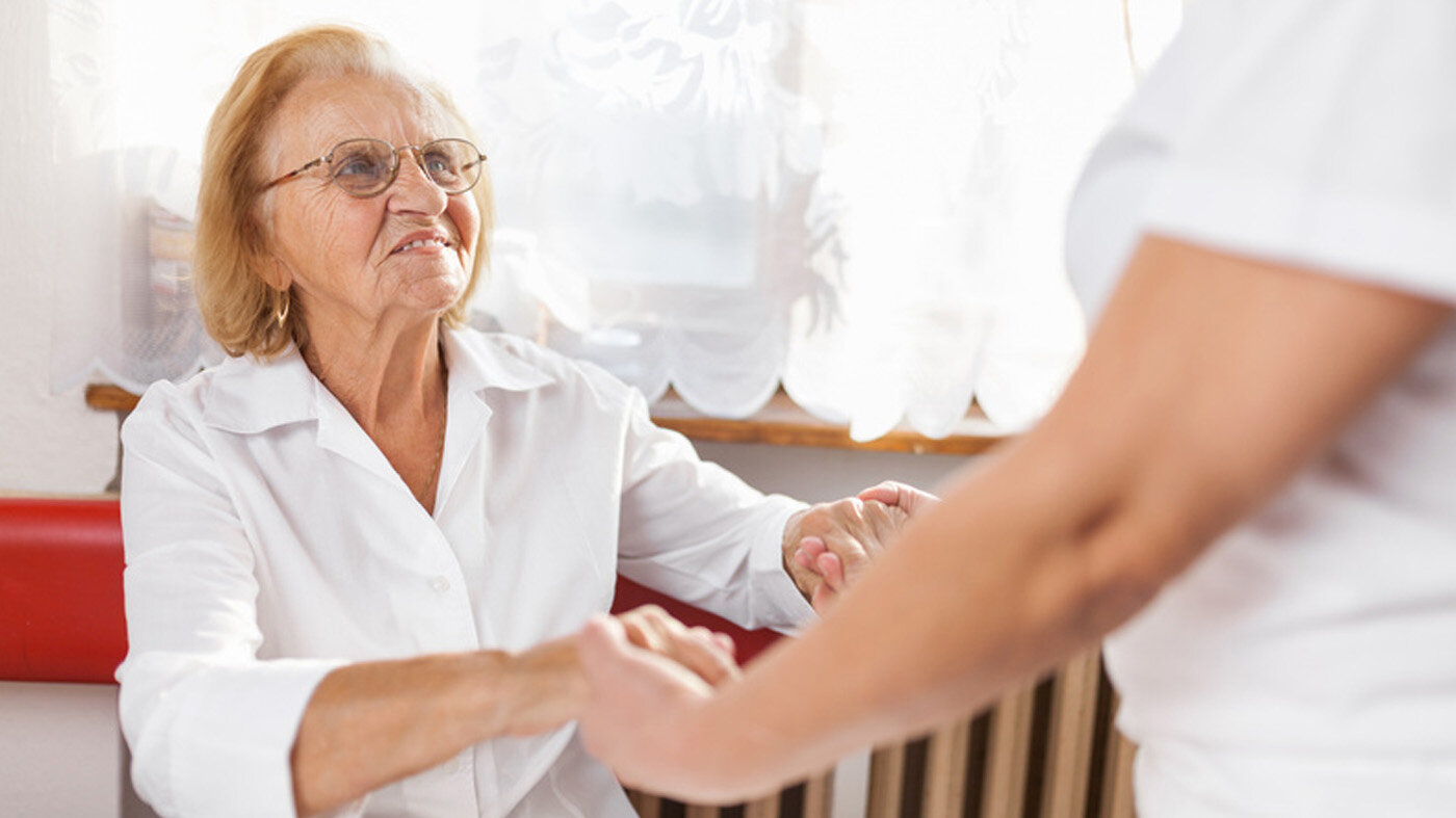 Bilde viser eldre dame som hjelpes av en pleier.