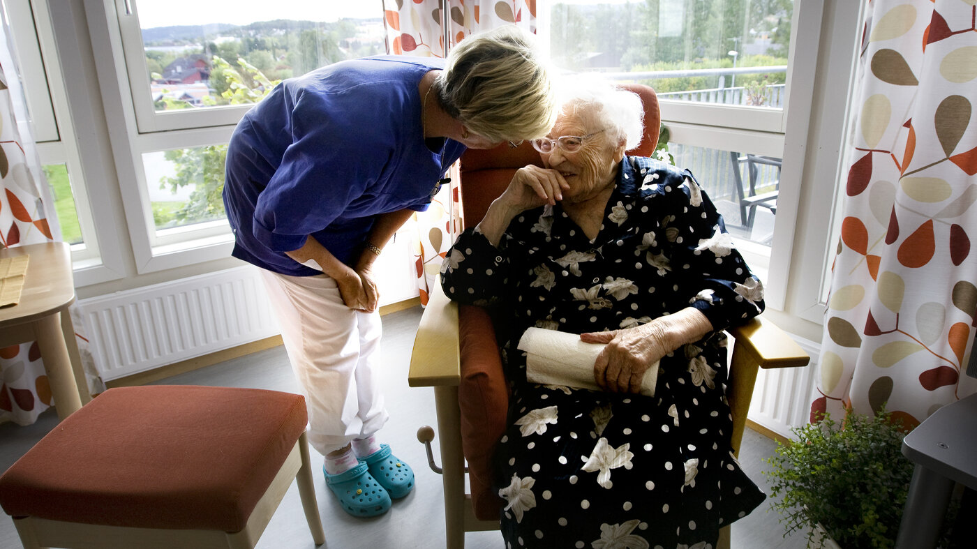 Bildet viser en eldre kvinne på velferdssenter. Får omsorg fra en av de ansatte.