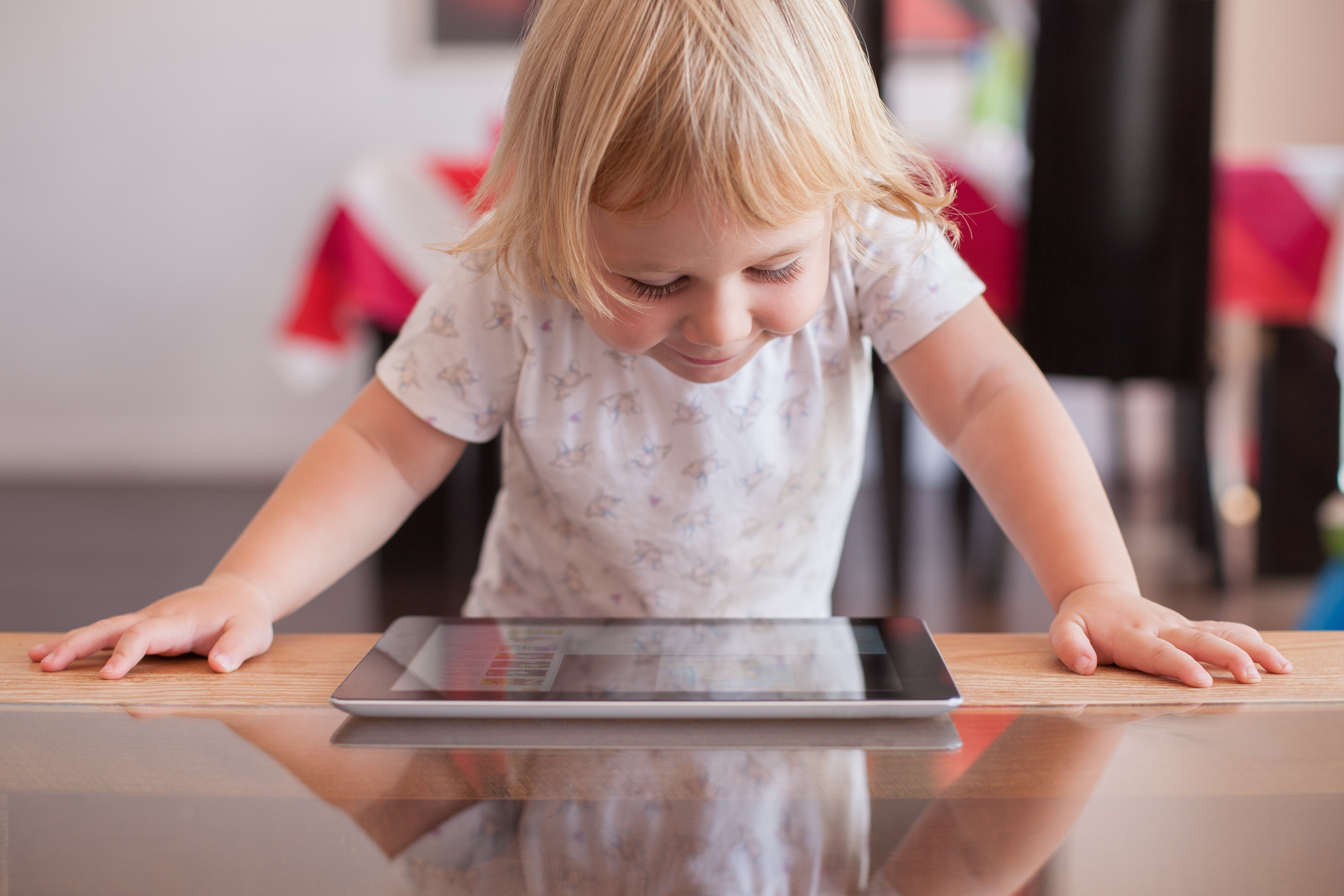 A smiling young girl looking down at a tablet on the table