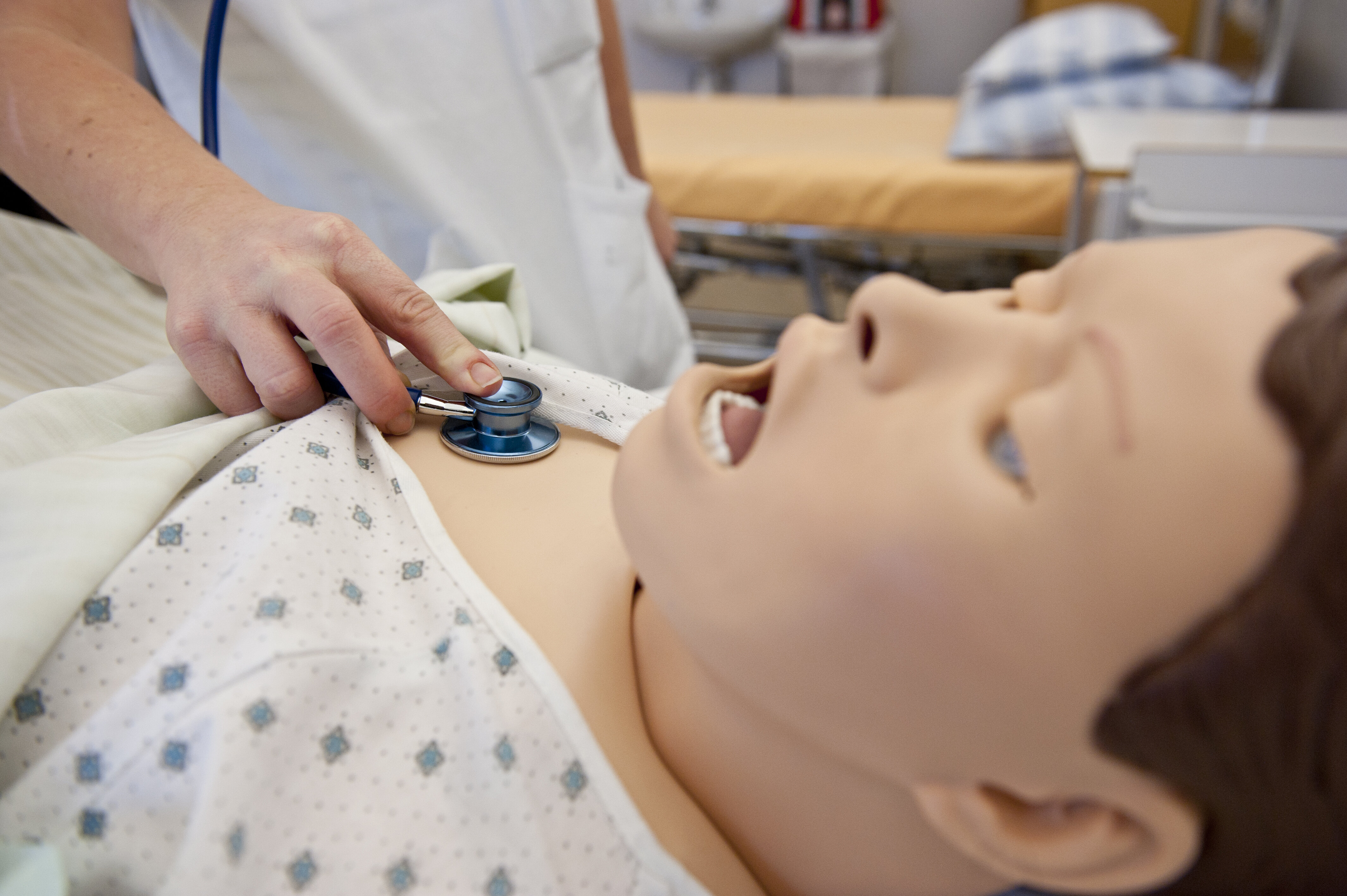Bildet viser en hånd som holder et stetoskop på brystet til en simuleringsdukke