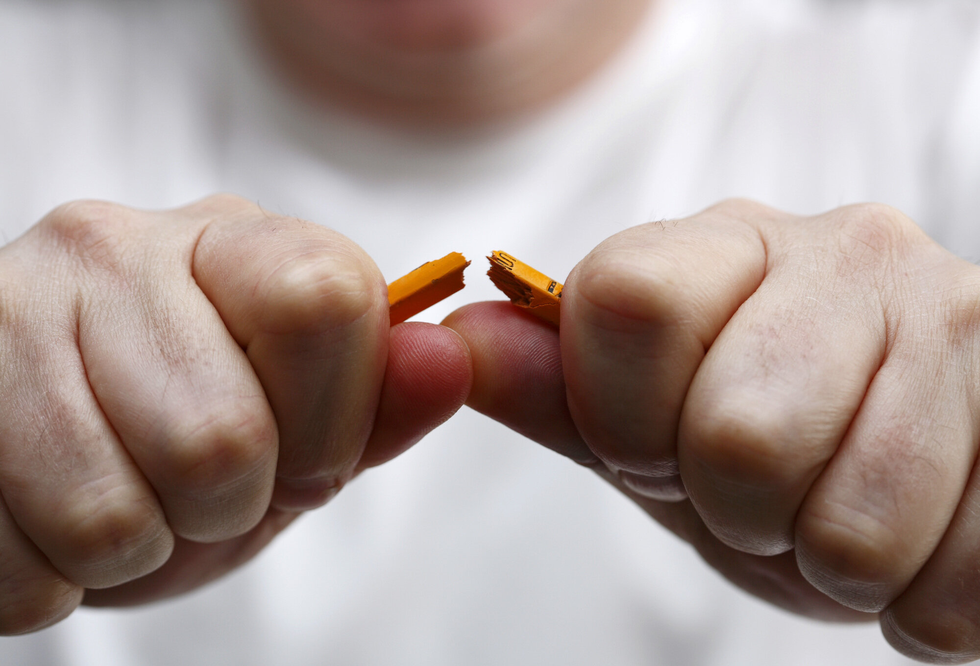 Nærbilde av at en mann knekker en blyant i to.