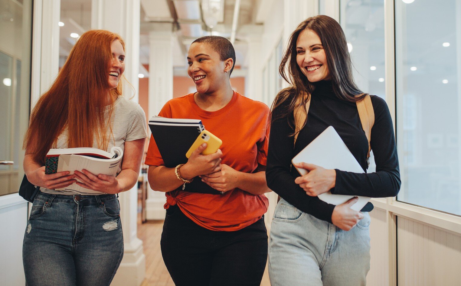 Bildet viser tre studenter som går i en gang på skolen og ler sammen