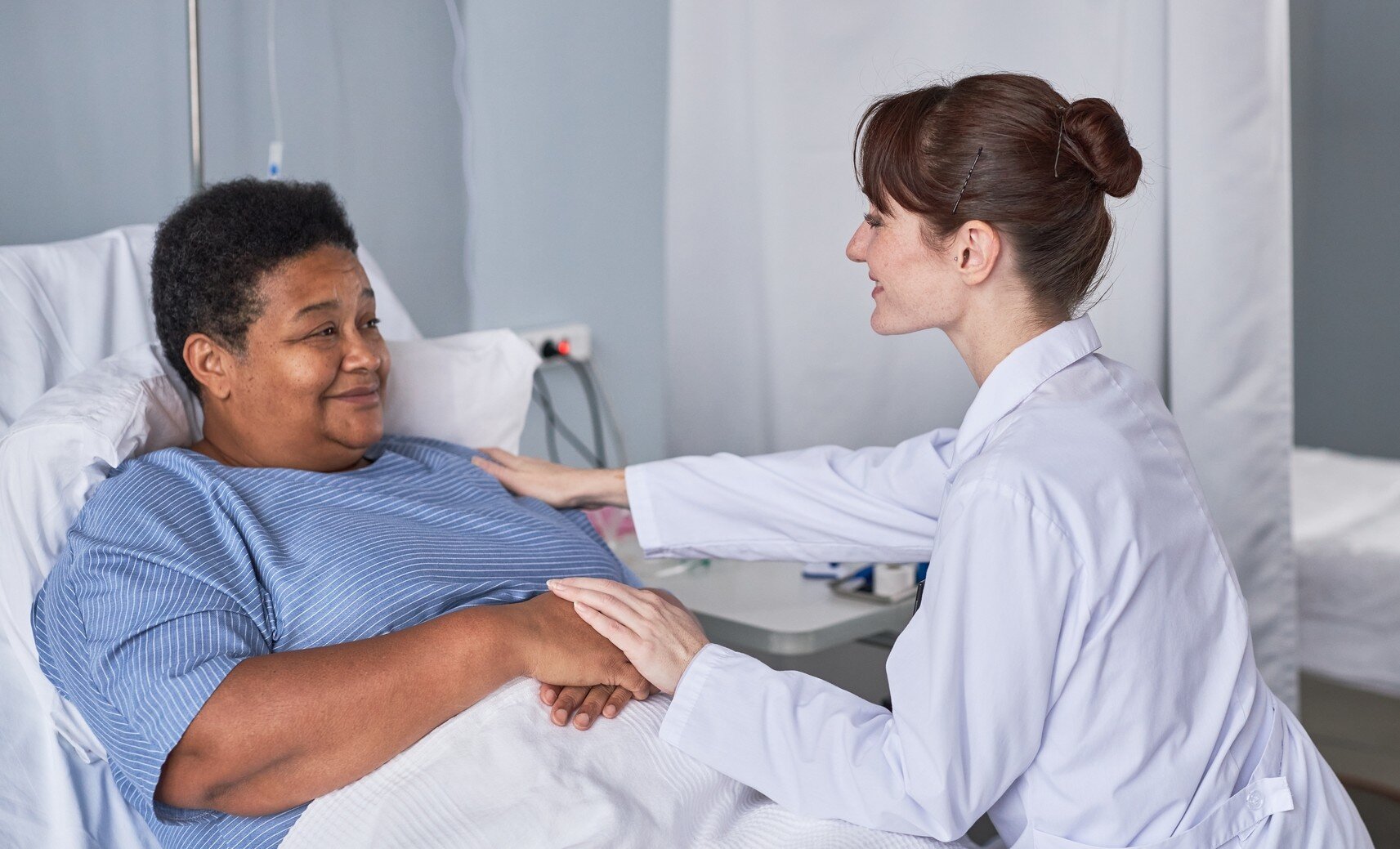 Bildet viser en sykepleier som trøster en pasient i sykehussengen
