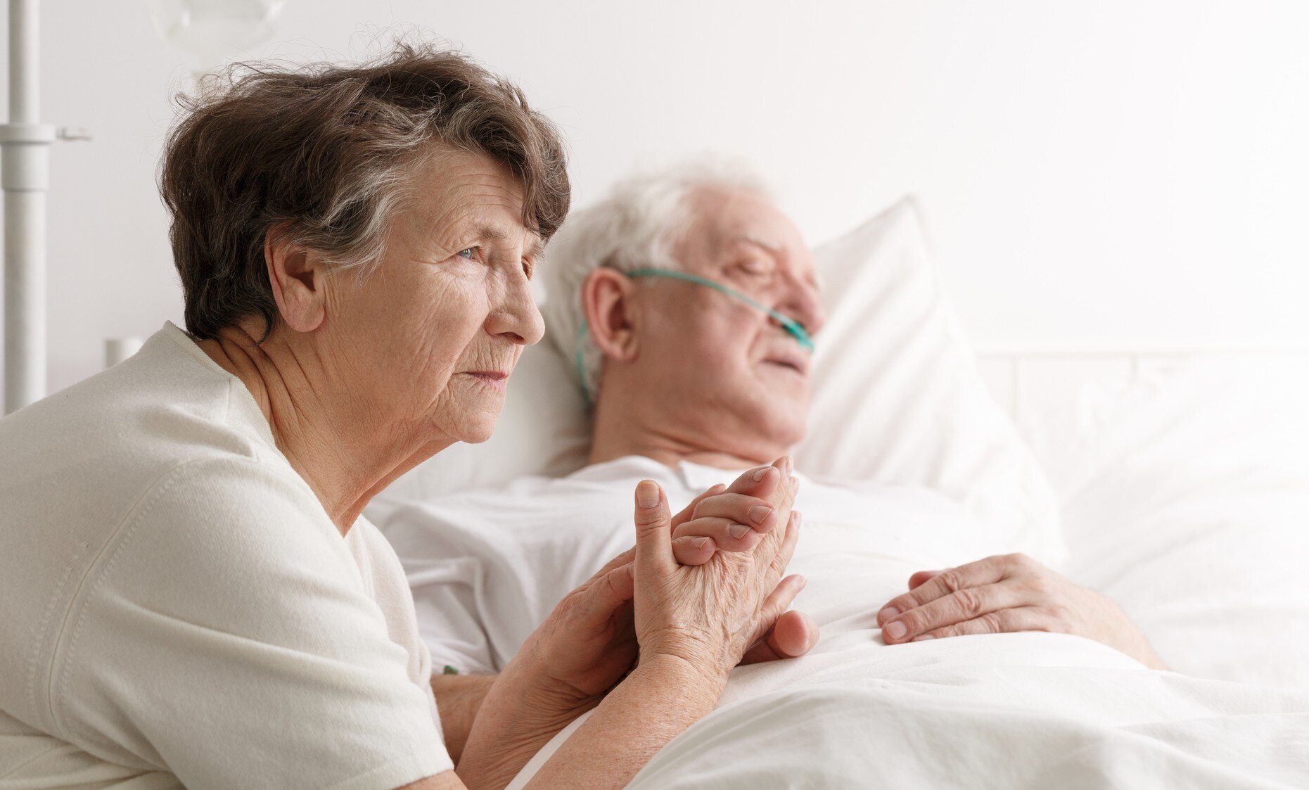 Bildet viser en kone som sitter ved sykesengen til sin døende mann