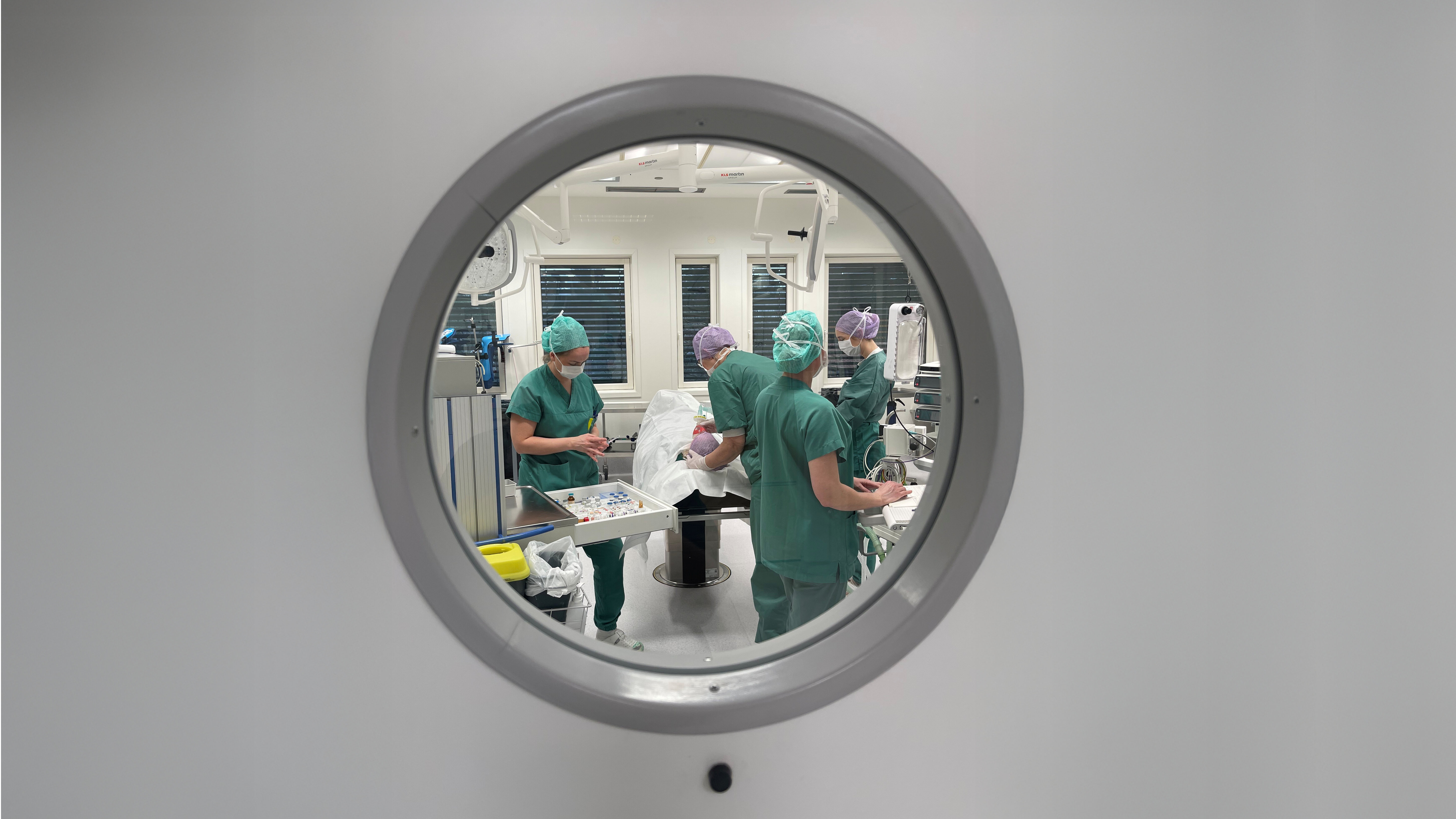 Bildet viser en dør med et rundt vindu inn til en operasjonssal. Gjennom vinduet kan man se flere sykepleiere i arbeid.