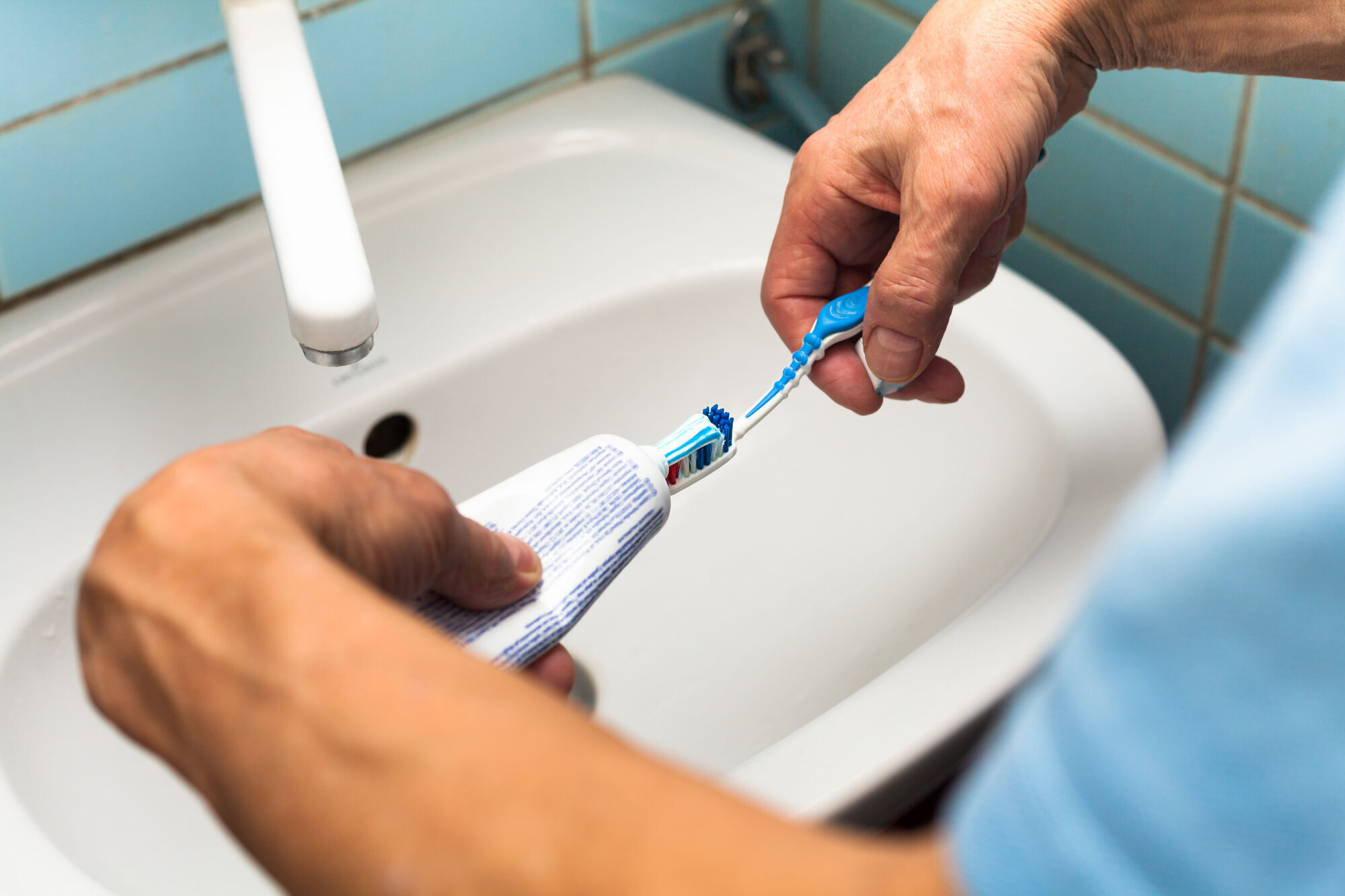 Bildet viser to hender som tar tannkrem på en tannbørste.