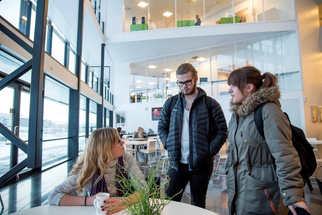 Bildet viser Anette Sagen som sitter ved et bord i kantinen og snakker med to medstudenter som står.