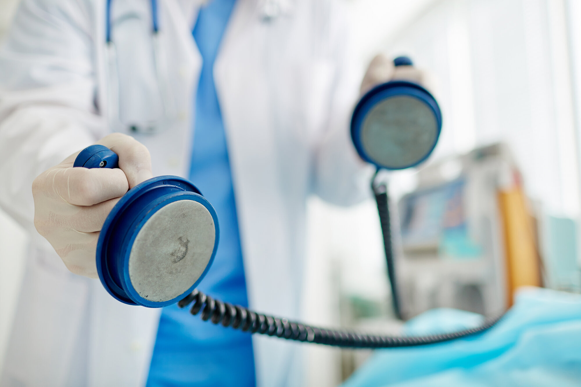 Bildet viser to hender som skal til å sette en defibrillator på en pasient