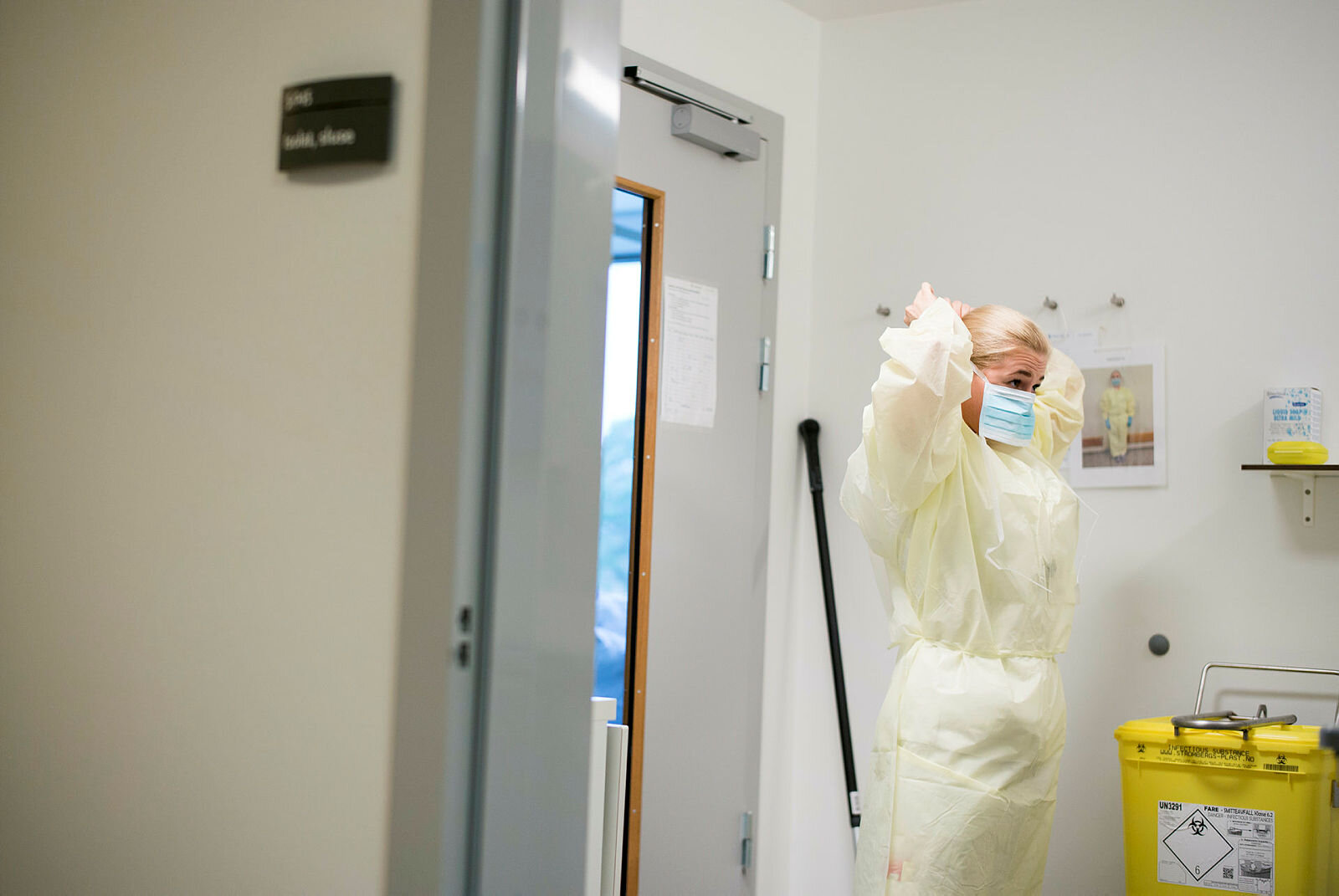 Bildet viser en sykepleier som står i en sluse inn til et isolat og tar på seg gul smittefrakk.