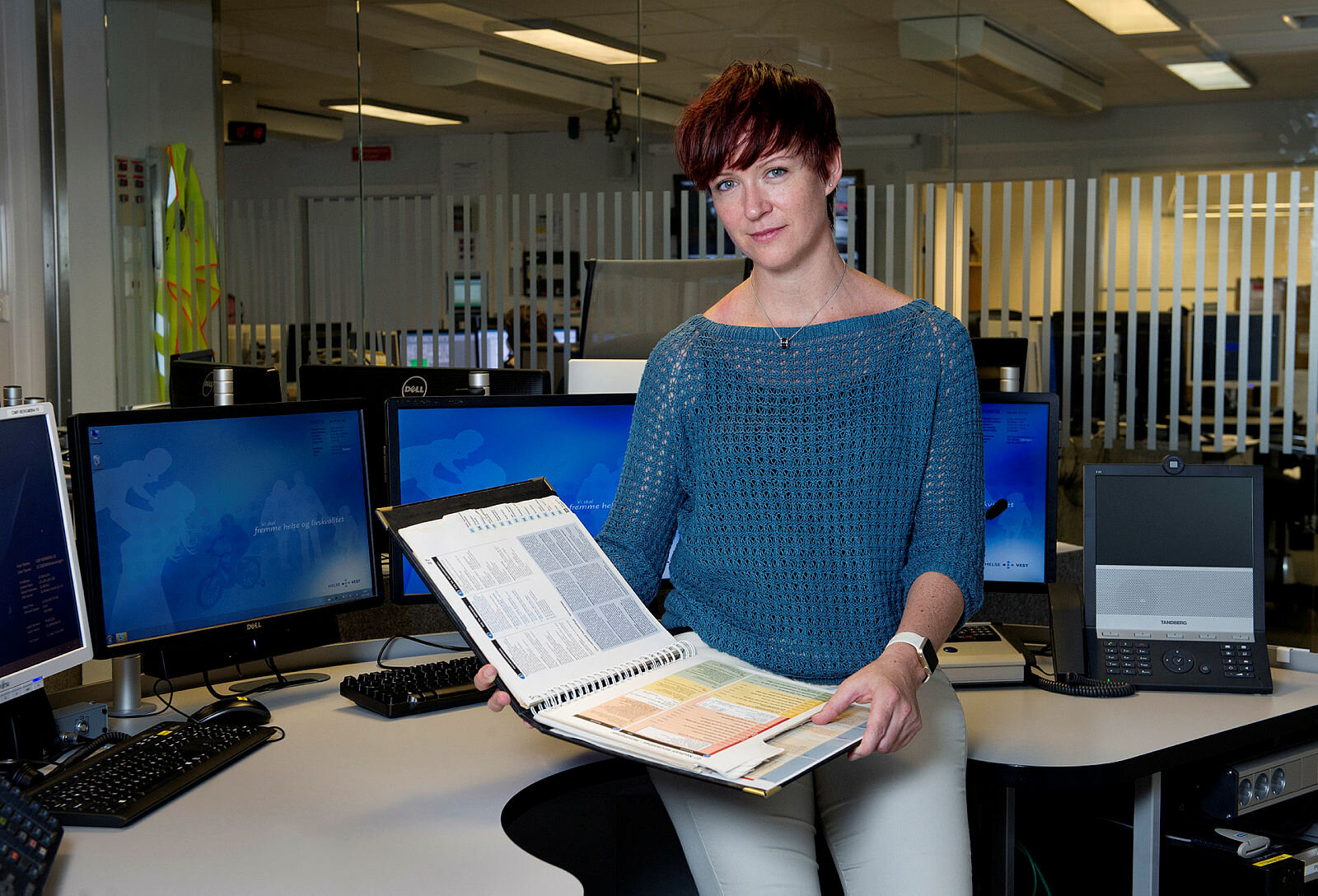 Bildet er et portrett av lege Eirin Ellensen på en AMK-sentral med Norsk indeks for medisinsk nødhjelp i hendene.