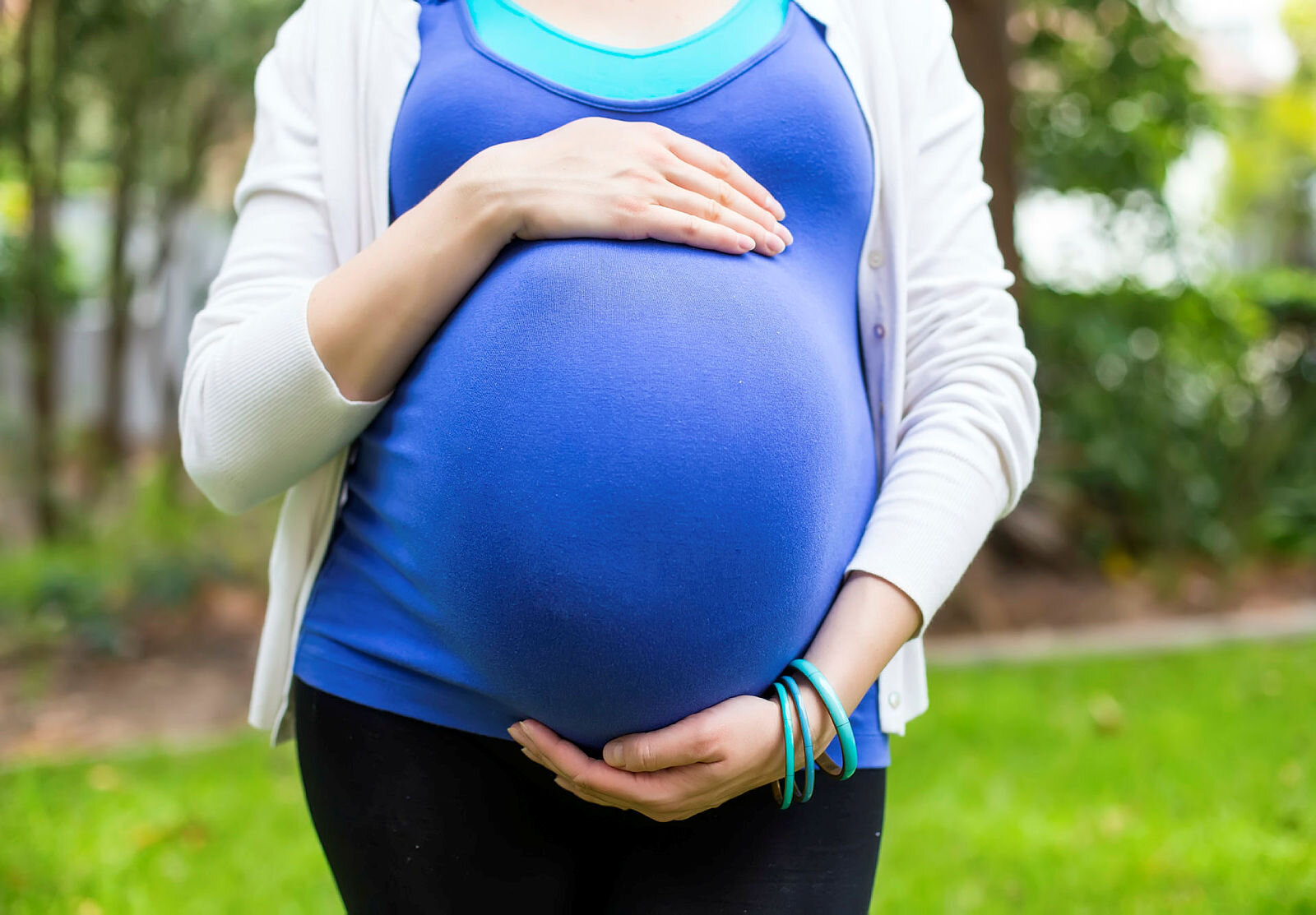 Bildet viser en gravid kvinne med blå topp som holder rundt magen sin
