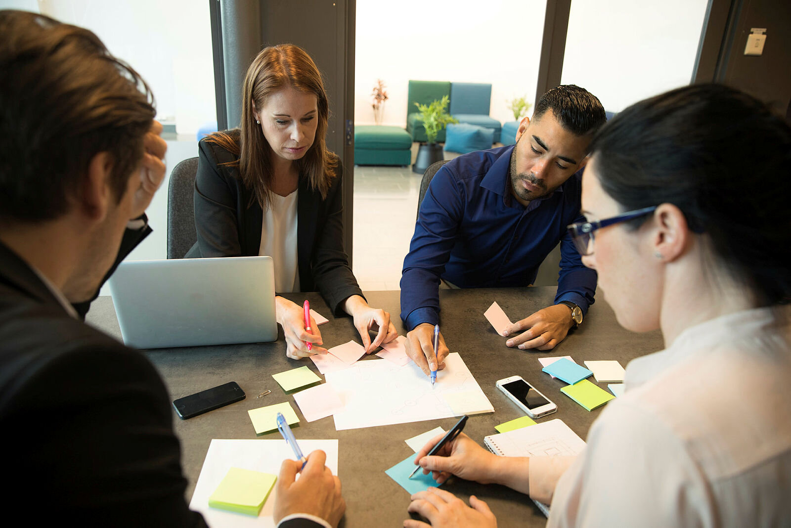 Bildet viser gruppearbeid på et kontor, der flere mennesker sitter rundt et bord med PC, ark og gule lapper foran seg.