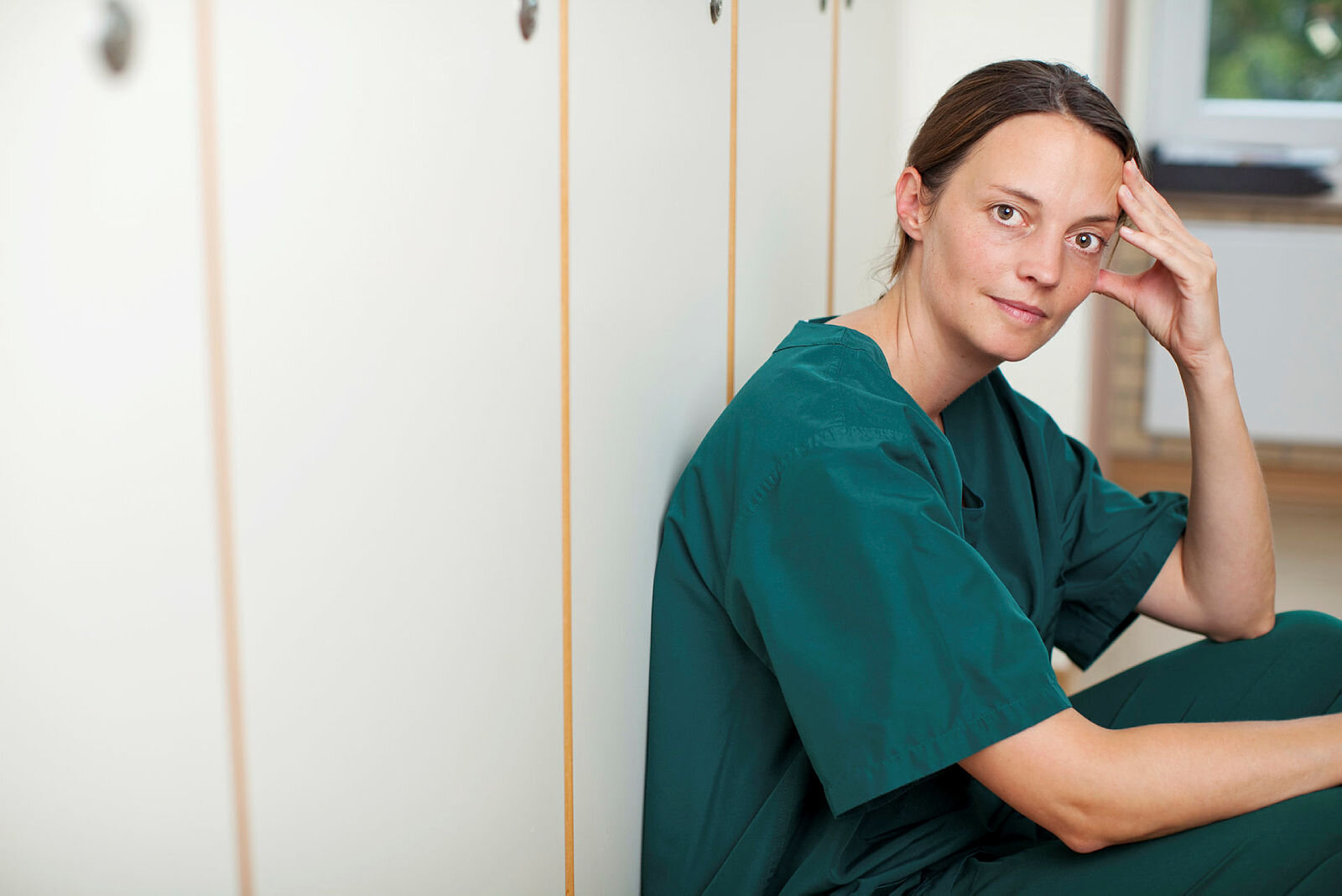 Bildet viser en sykepleier som sitter i en gang og ser tankefull ut