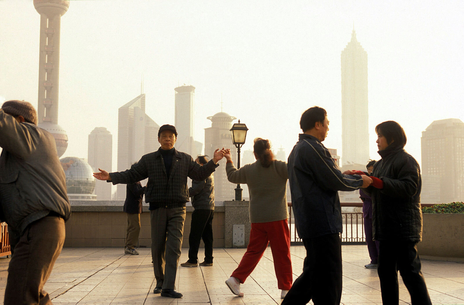 Bildet viser en gruppe eldre mennesker i Shanghai som gjør en form for morgengymnastikk med byen i bakgrunnen.