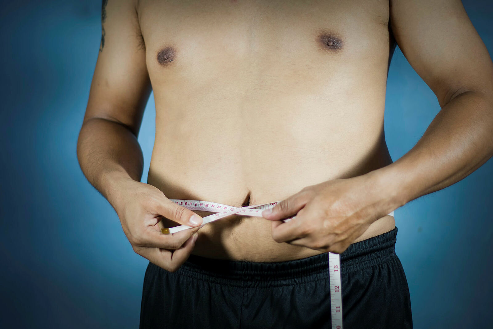 Bildet viser en litt tykkfallen mann som måler midjen med et målebånd.
