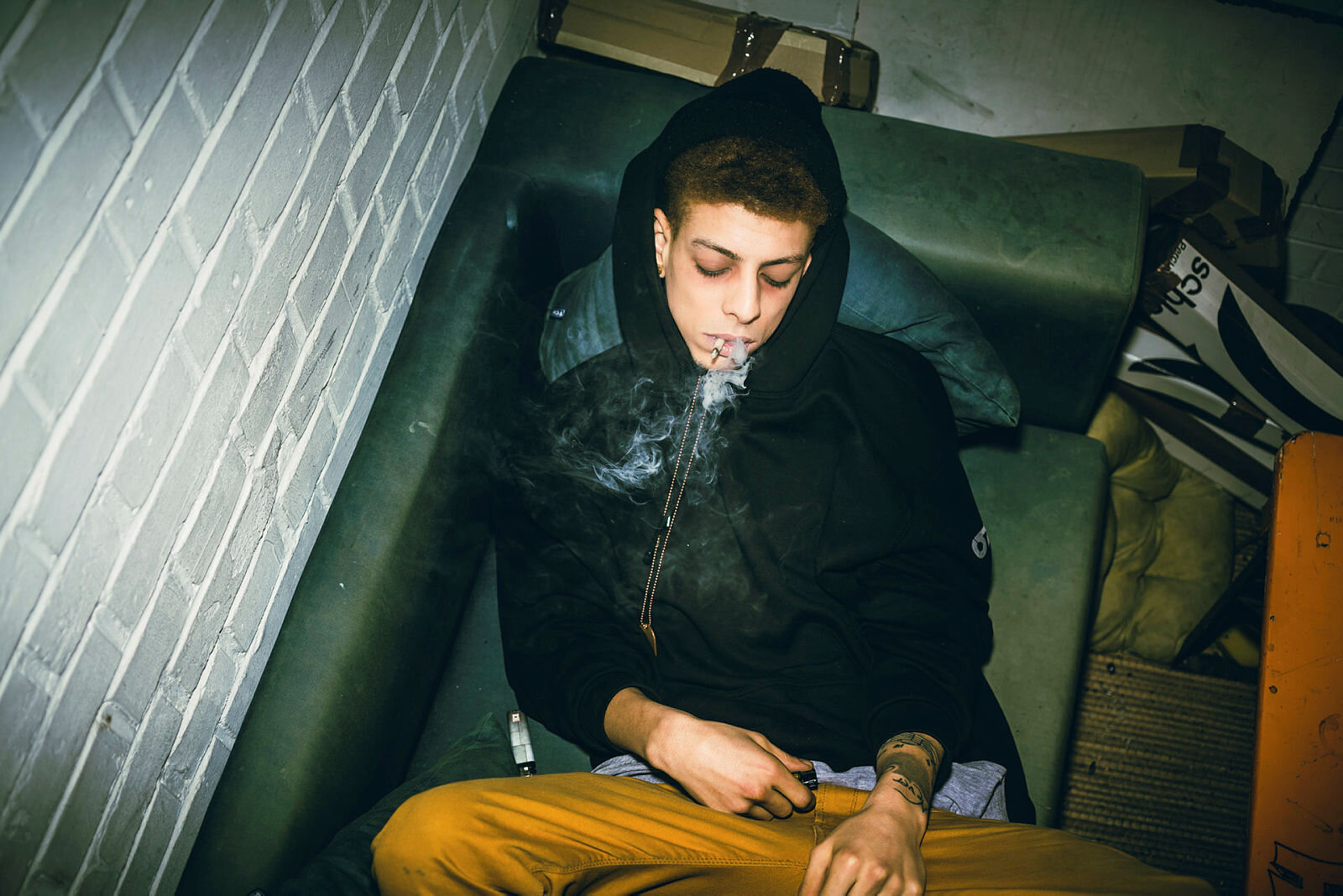 Bildet viser en ung mann som ligger på en sofa og røyker en joint