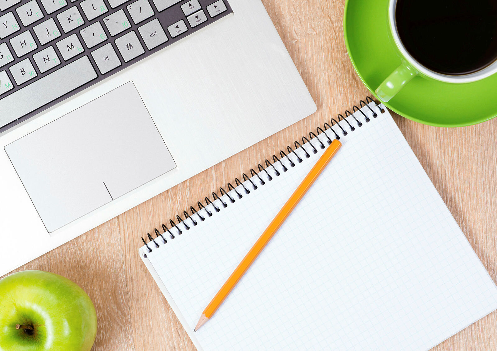 Bildet viser deler av en bærbar PC, en skriveblokk, et eple og en kaffekopp.