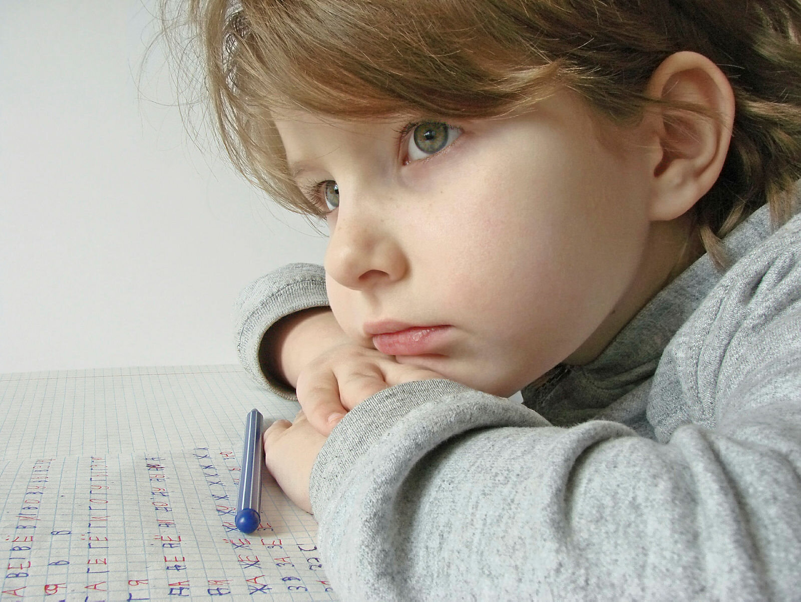 Bildet viser en tankefull jente som øver på å skrive bokstaver på et papir.