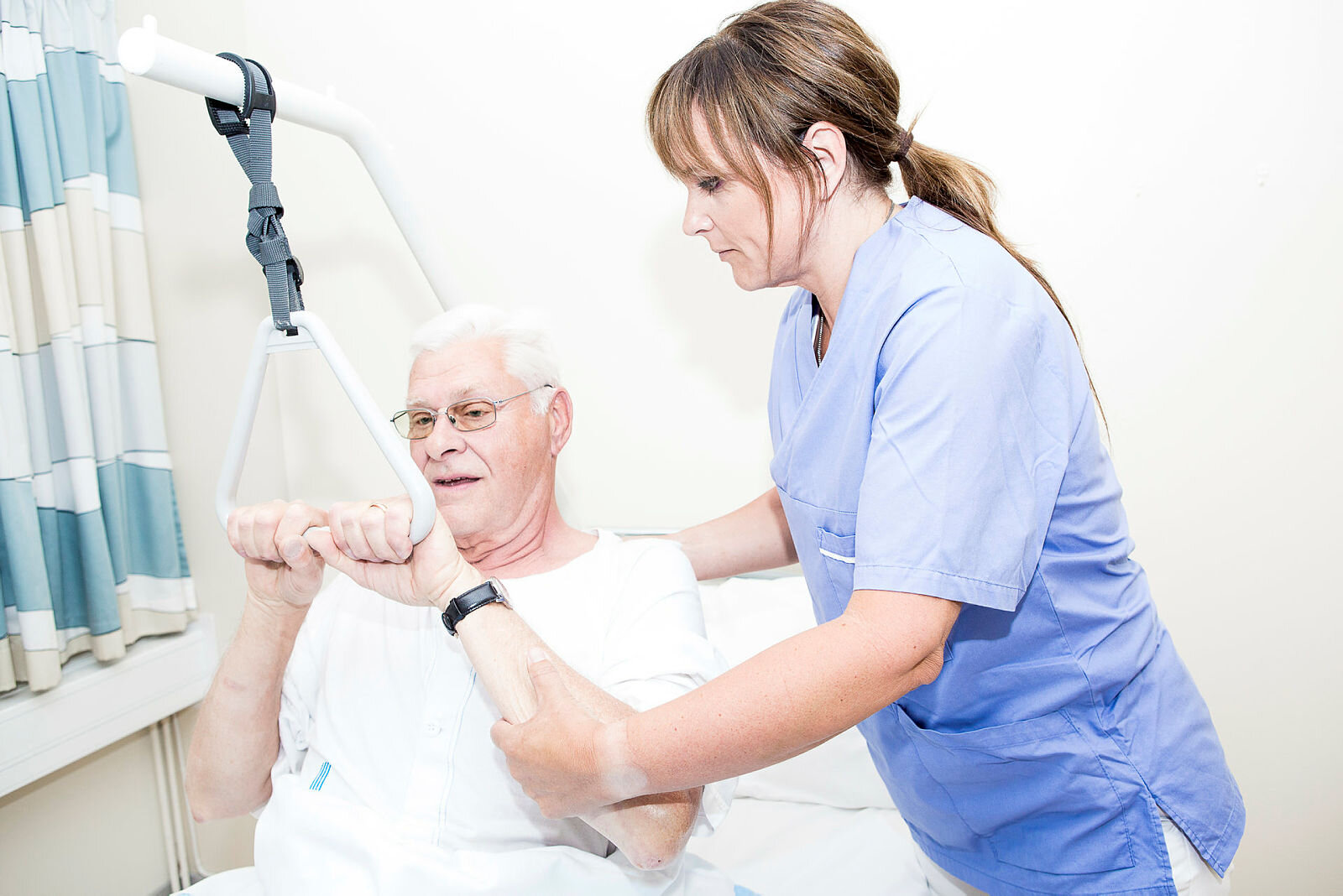 Bildet viser en sykepleier som hjelper en eldre mann med å sette seg opp i sengen