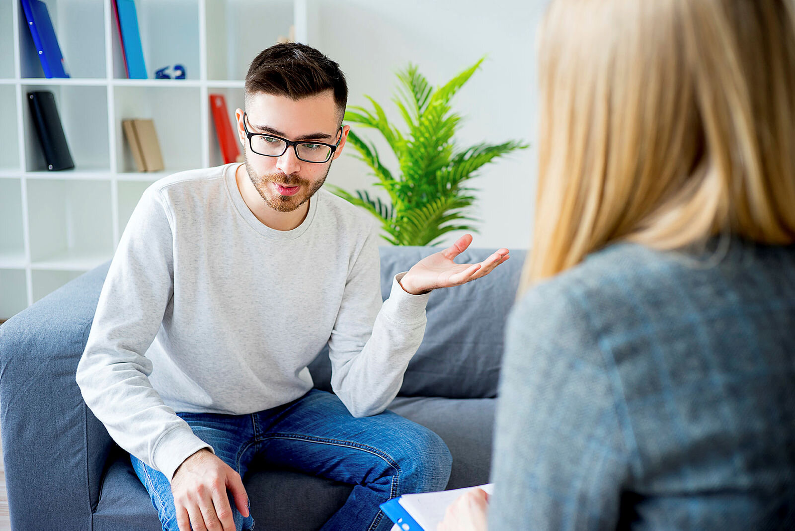 Bildet viser en ung mann som sitter i en sofa, tvers overfor en kvinnelig terapeut, som vi ser ryggen av.