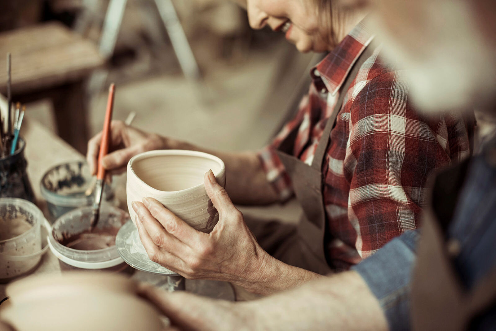 Bildet viser en eldre kvinne og en eldre mann som lager og dekorerer gjenstander i leire