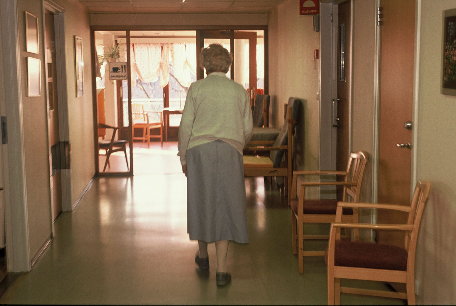 Eldre kvinne går nedover sykehjemskorridor
