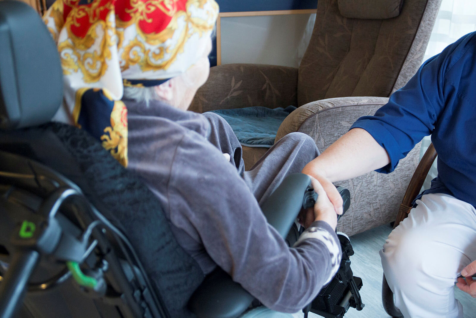 En gamel dame som sitter i en stol og holder en pleier i hånden.