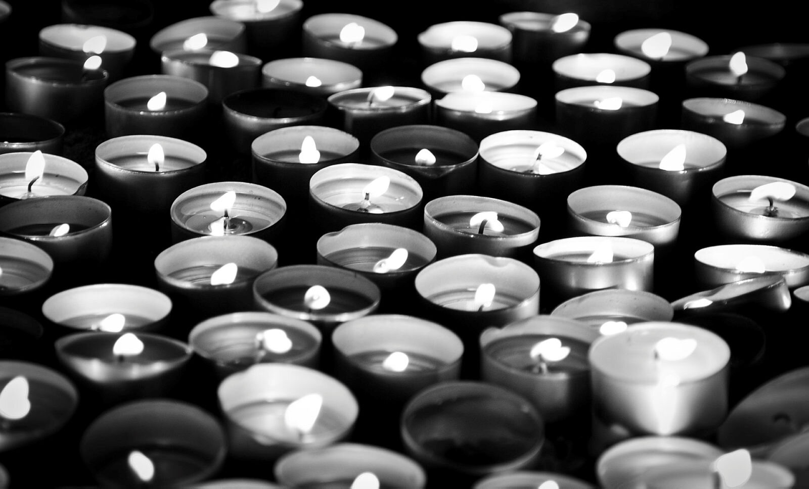 Bildet er svart-hvitt og viser mange telys som holder på å brenne ut